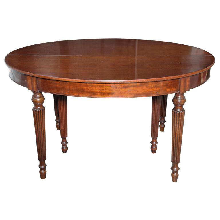 An oval English solid mahogany dining table with six reeded legs below apron with molded edge, the top opening to accommodate three later mahogany leaves with aprons. This lovely piece showcases wood of a warm, walnut coloring, circa 1950.

This