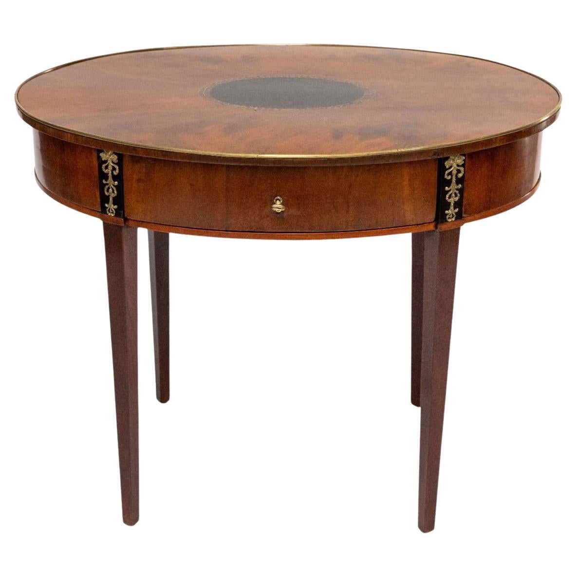 Danish empire mahogany sewing table, expertly crafted with refined quality. The oval tabletop features a gilded bronze edge, with a central black-polished oval inlay adorned with gilded bronze detailing.
The table includes a drawer within the apron,