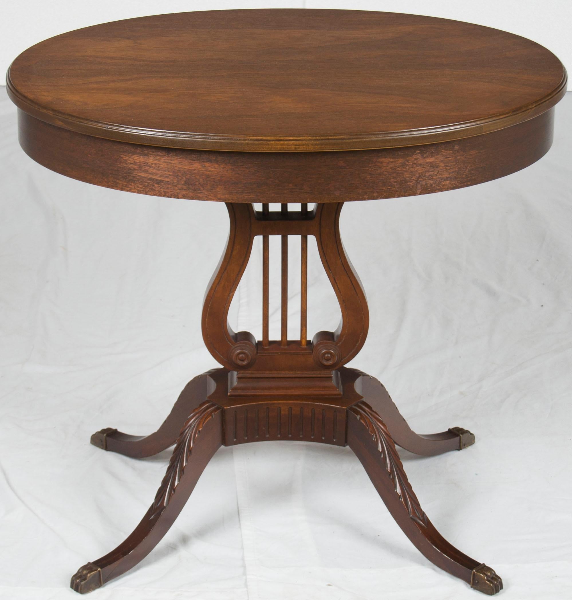 American, this mahogany accent table features a medium brown, smooth finish in very good condition. The spacious oval table top transitions beautifully to the lyre shaped trestle and splayed legs. The splayed legs are connected by a platform that