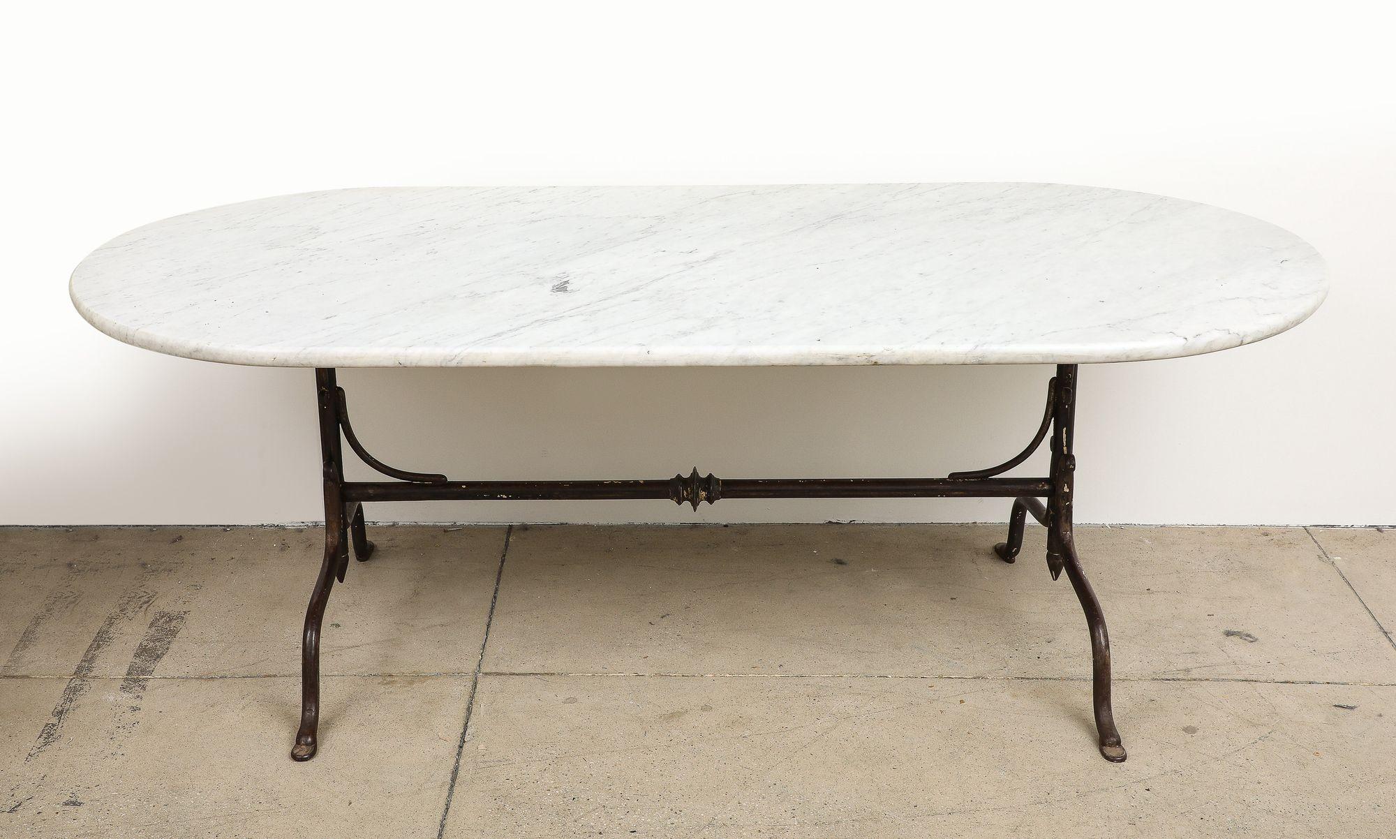 A mid 20th Century French dining table features a graceful white marble oval shaped top with an iron trestle base. Elegance meets functionality in a captivating outdoor dining table. This table exudes timeless charm, working beautifully in a home,