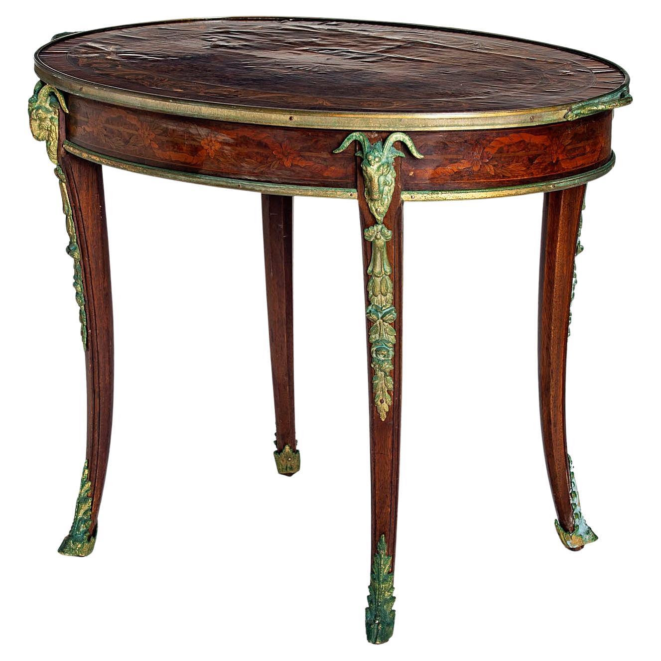 Antique oval occasional table with elaborate marquetry & inlay design. Mythical ormolu mounts in brass with natural patinaed finish in shades of blues & greens with elaborate detail throughout. Some of the veneers have buckling & have been repaired,