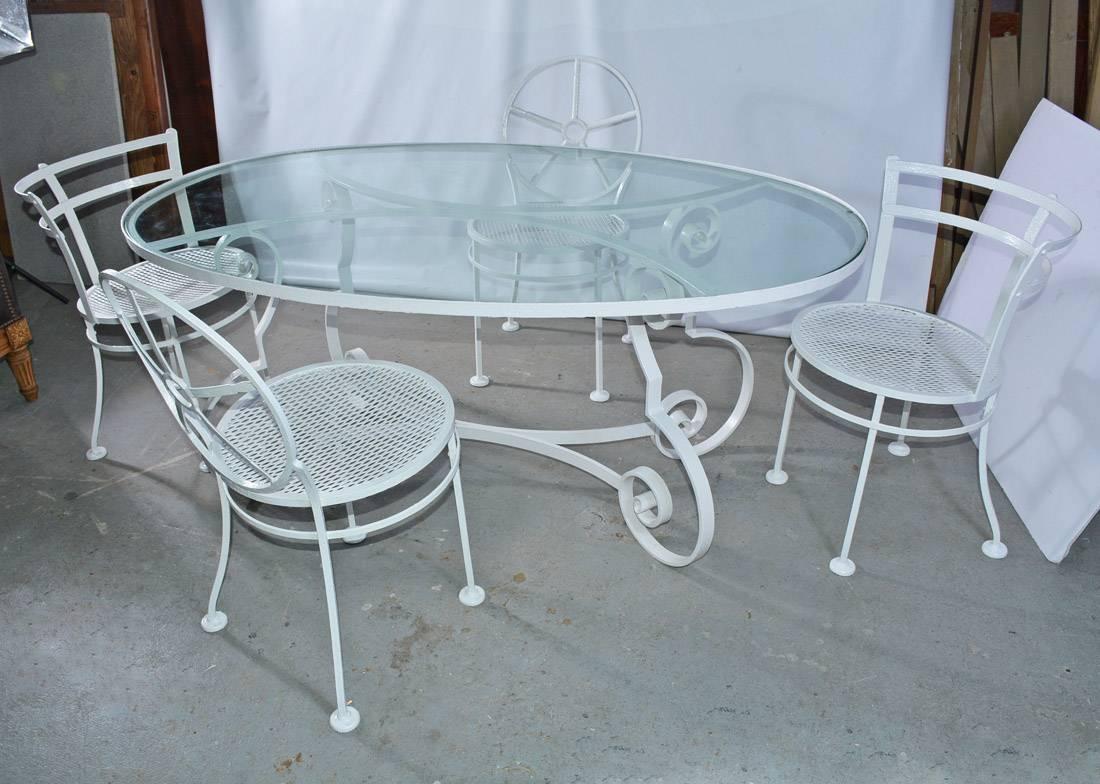 Indoor or outdoor oval metal and glass mid-century Patio/Porch garden table and four dining chairs. Dining table has an iron base and glass top. The base is designed with Baroque scroll legs and curved braces that match the curved braces supporting