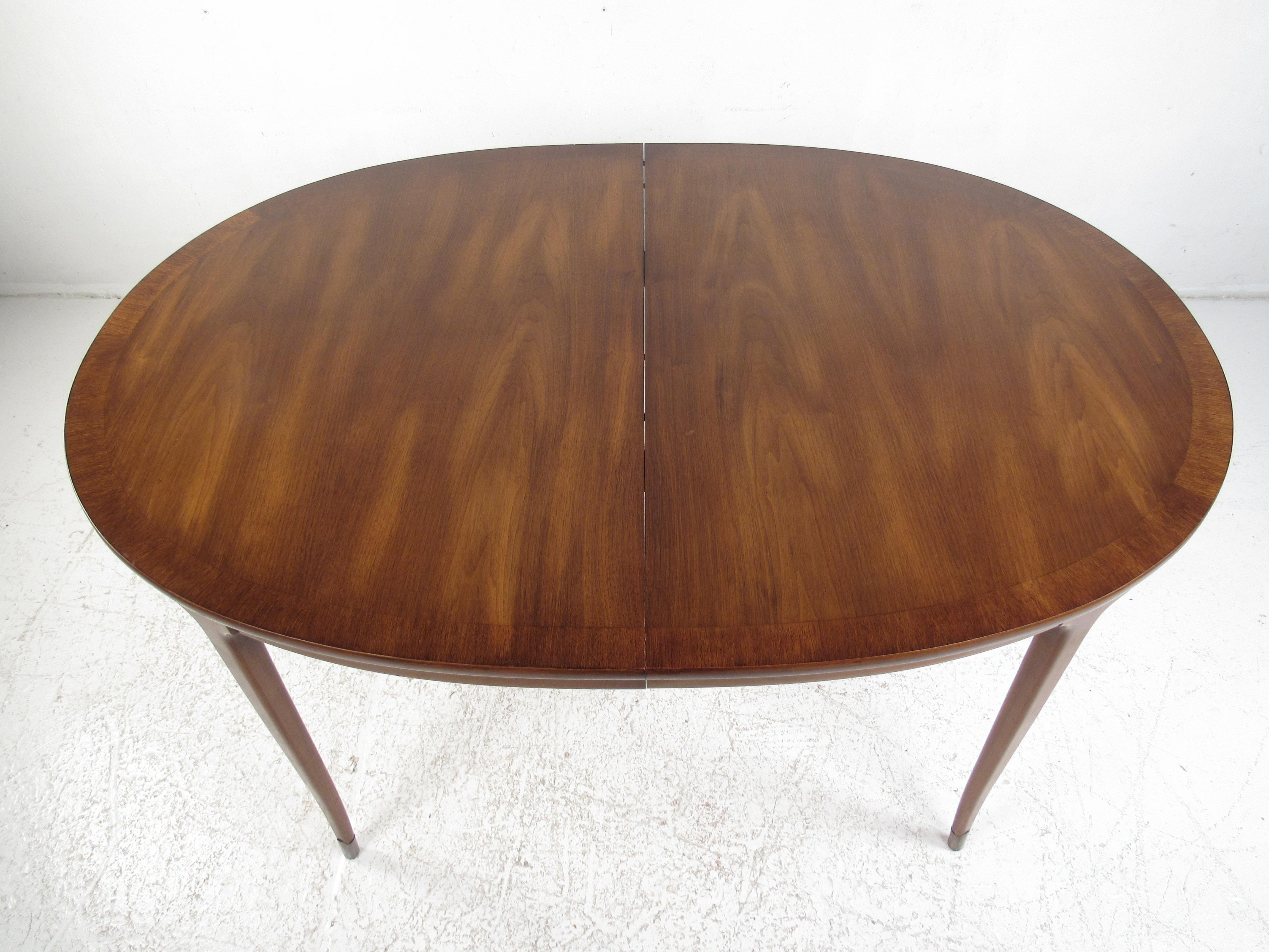 This beautiful vintage modern dining table boasts an oval top and long tapered legs with brass feet. A sleek design that extends from 58 inches wide to 90 inches wide, ensuring plenty of room for guests. Sturdy construction with elegant walnut wood