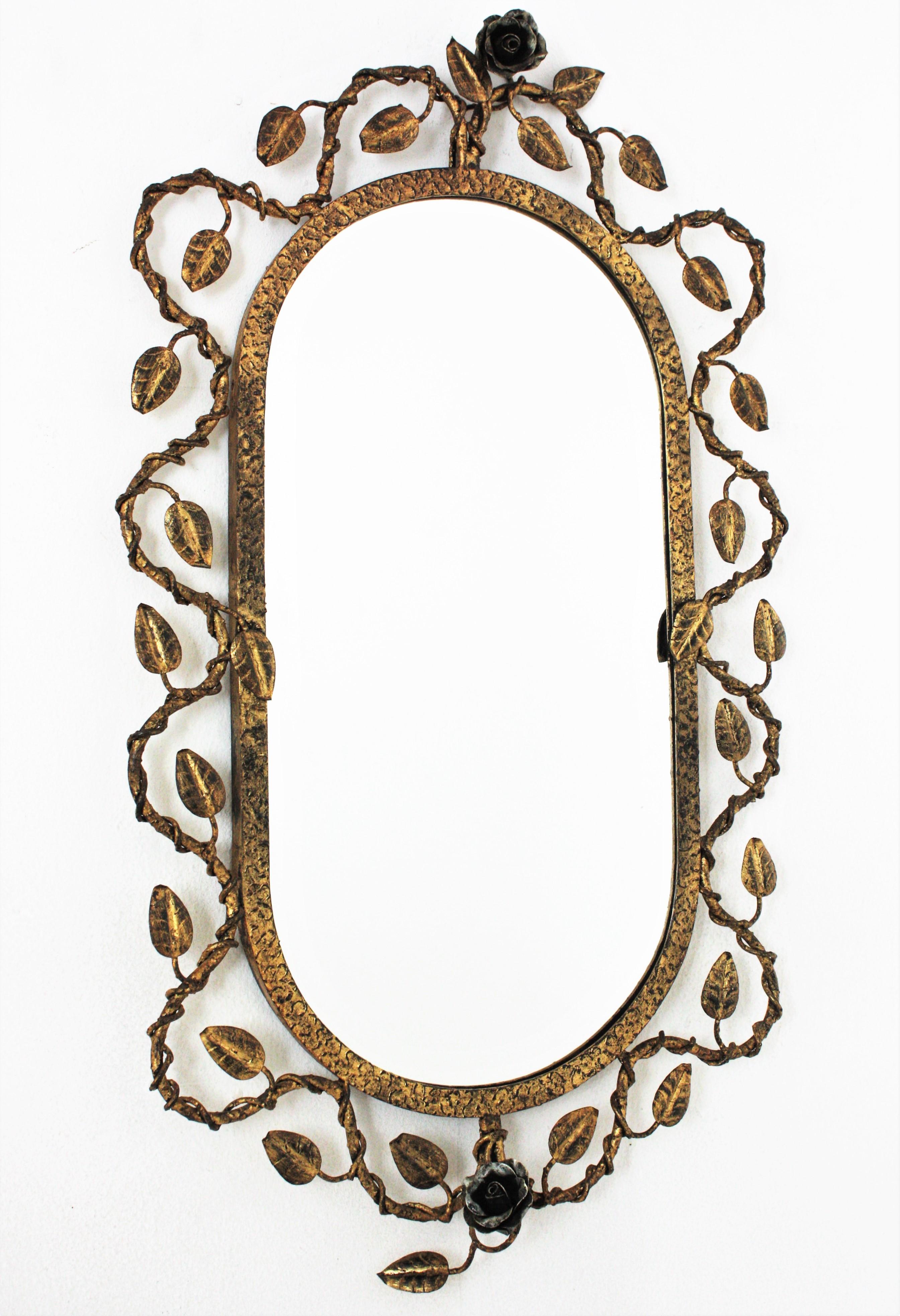 Foliage Floral Oval Mirror in Gilt Hand Forged Iron, Spain, 1950s.
Hand wrought iron oval sunburst wall mirror with foliage frame , gilded finish and floral accents in silvered iron. 
The frame features and intrincate of branches and leaves with