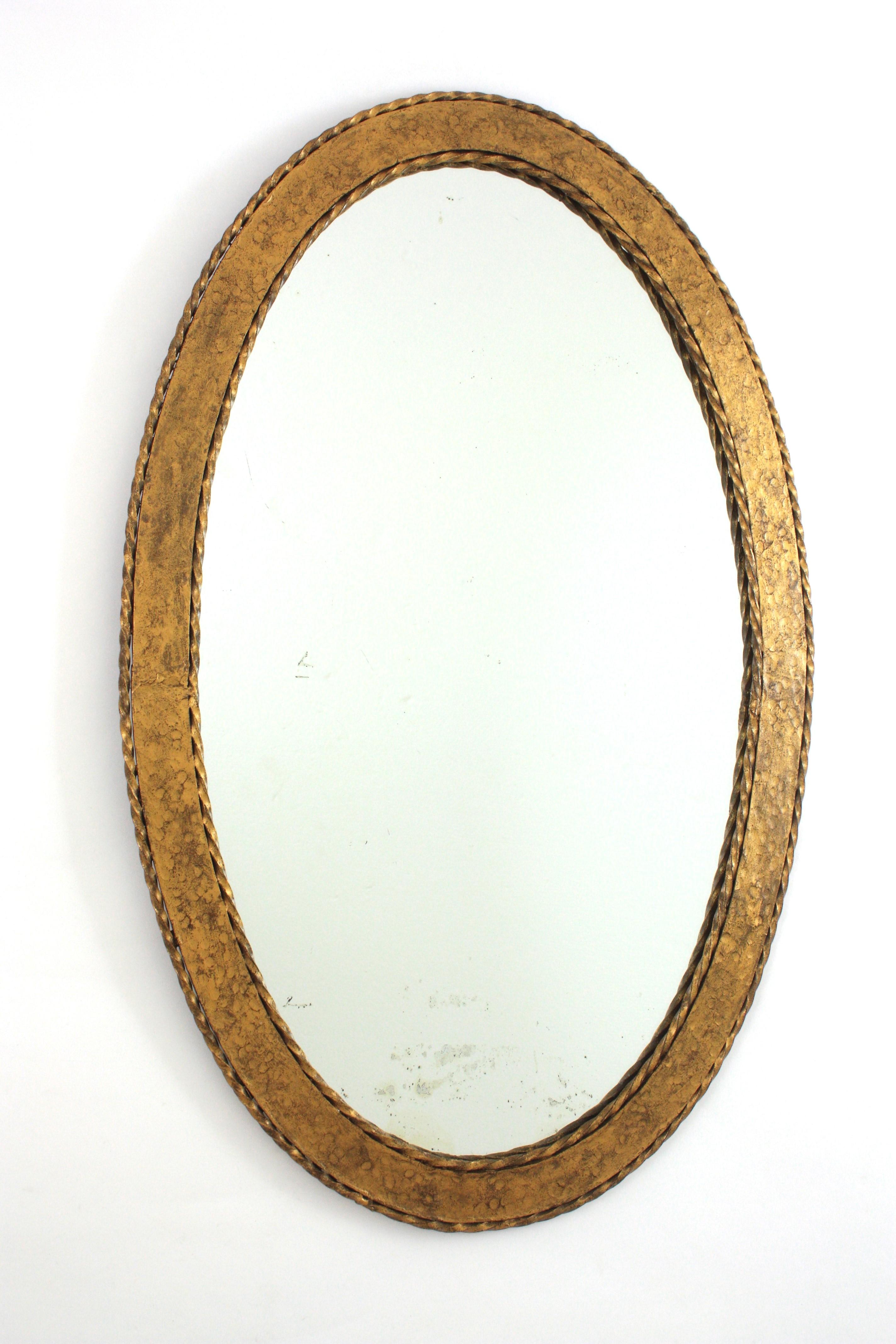 Miroir ovale doré, fer, Espagne, années 1950
Ce miroir ovale attire l'attention par son cadre en fer forgé à la main, ses détails en corde de fer torsadée et sa patine dorée. Lourdement orné par les marques de marteau minutieuses. 
Ce miroir est en