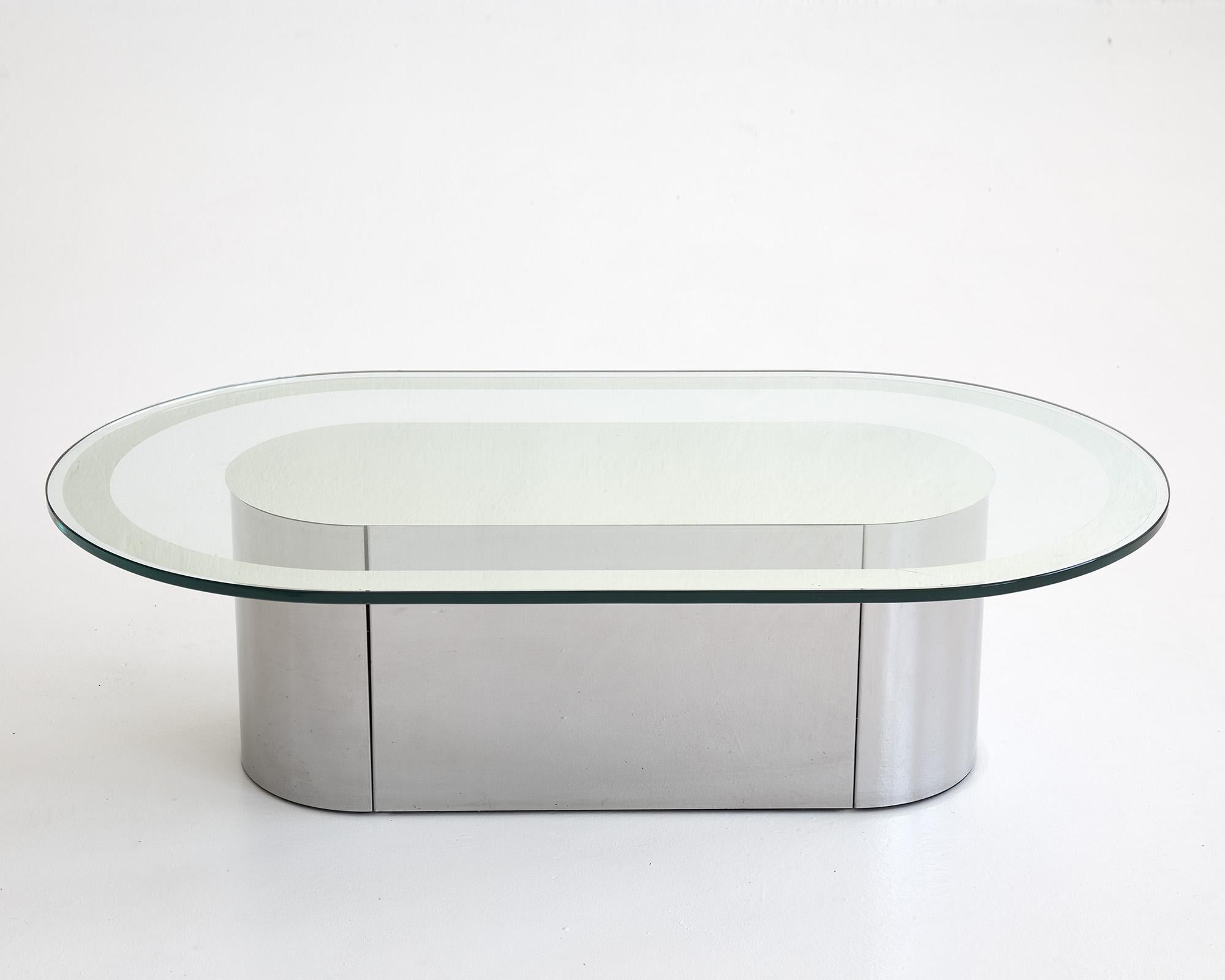 Table basse très élégante et de grande qualité, probablement fabriquée en Italie vers 1970.

Le plateau ovale en verre présente un motif incurvé incrusté composé de deux lignes qui créent un effet d'optique intéressant.

La base en métal poli miroir