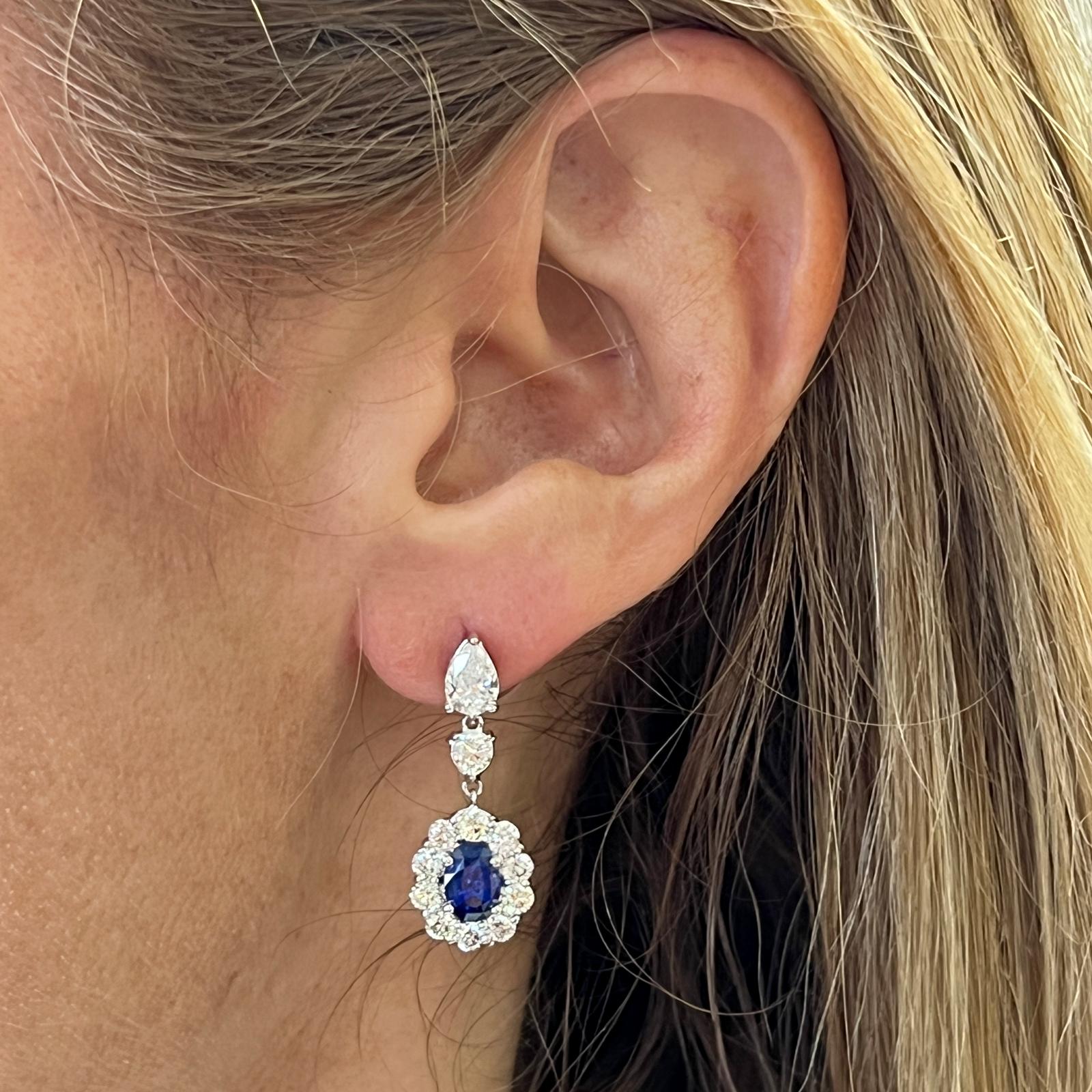Timeless sapphire diamond drop earrings fashioned in 18 karat white gold. The earrings feature 2 oval natural blue Ceylon sapphires weighing 1.54 carat total weight. The sapphires are surrounded by 22 round brilliant cut diamonds weighing 1.91 CTW,