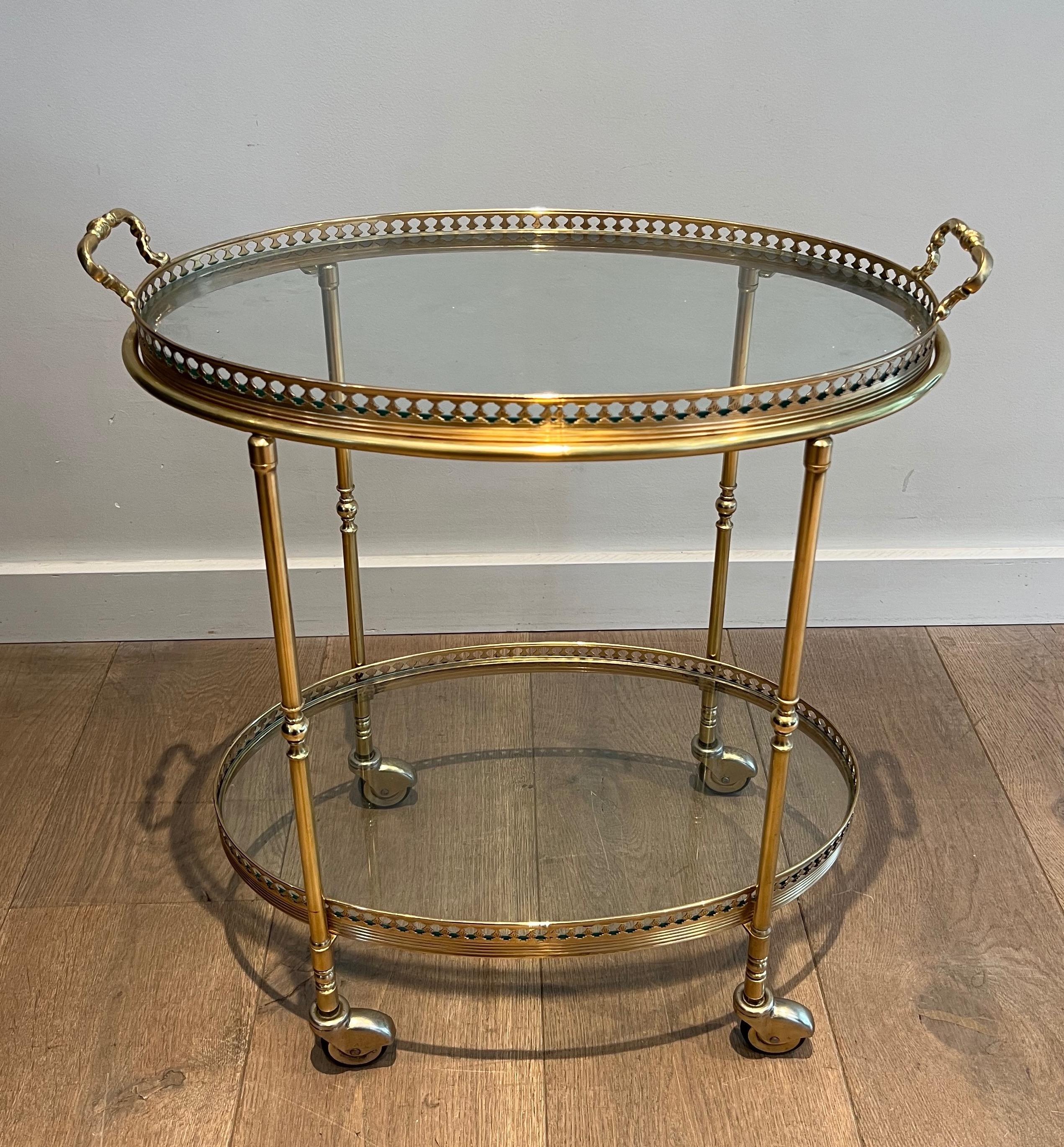 This very nice and elegant neoclassical style oval bar cart is made of brass with 2 glass trays. The top glass trays is removable and can be used to serve. This is a fine French work attributed to Maison Jansen. Circa 1940