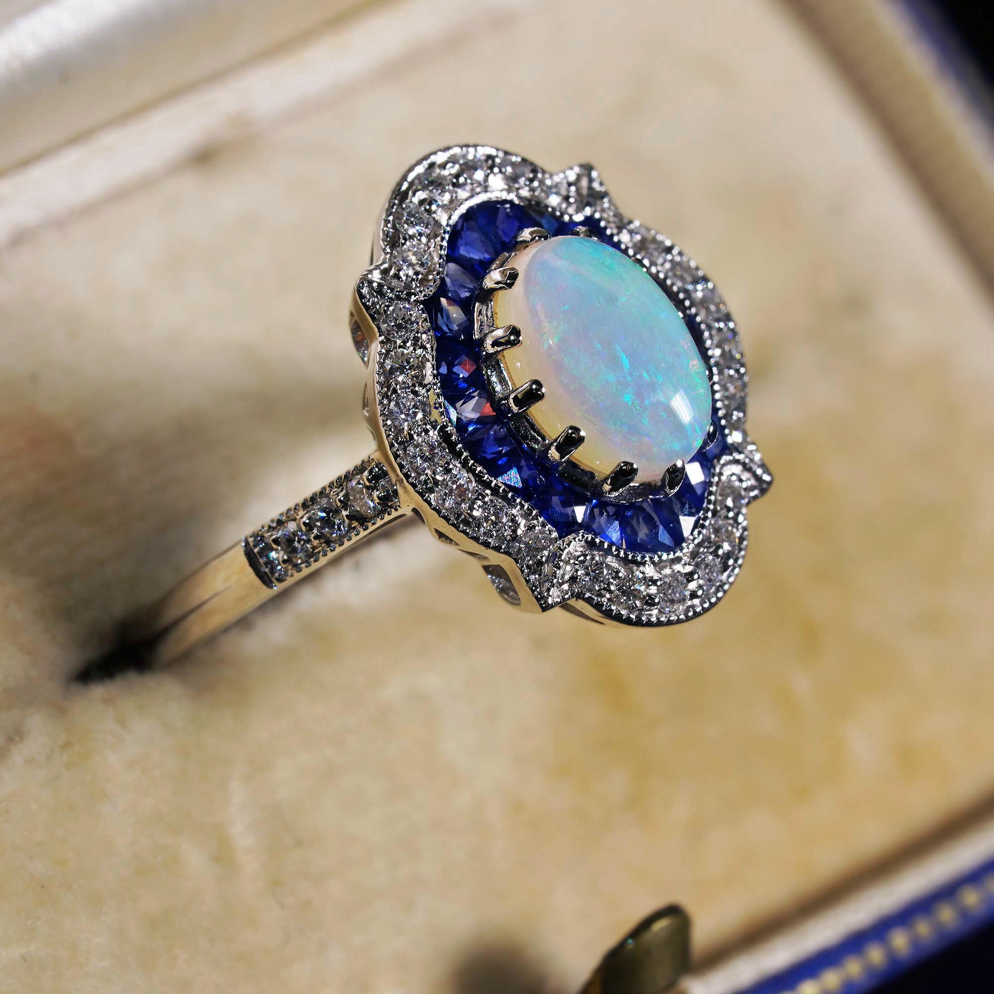 A totally unique opal, sapphire and diamond cluster ring of exceptional design. The center prong set with a magical natural opal displaying rainbow like hues. The opal is surrounded by a halo of French cut blue sapphires and sparkly diamonds in a