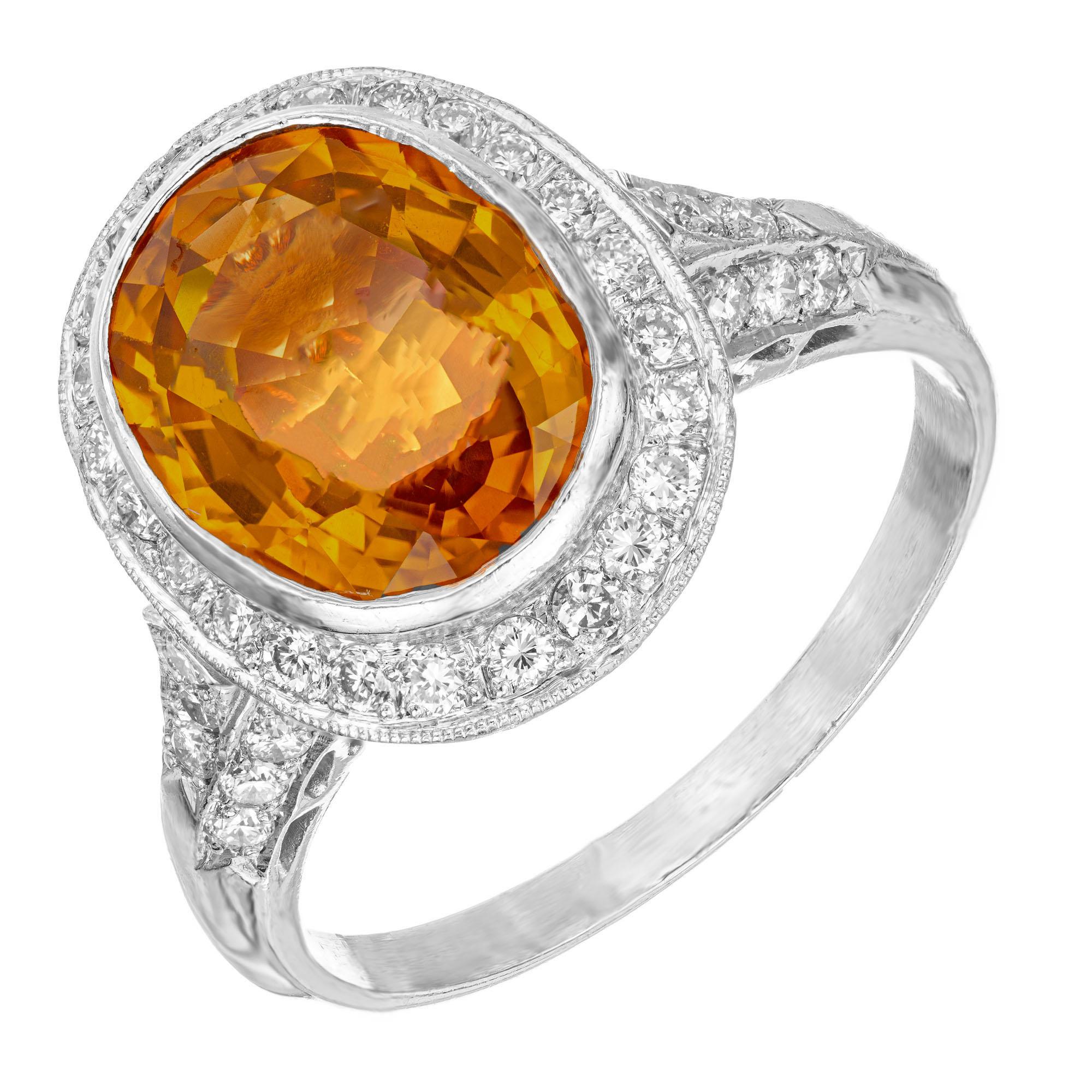 1970's Orange sapphire and diamond engagement ring. 4.00ct. certified oval orange center sapphire, in a bezel set platinum setting with a halo of full cut diamonds, accented with micro pave accent diamonds along the shank and crown. This AGTA