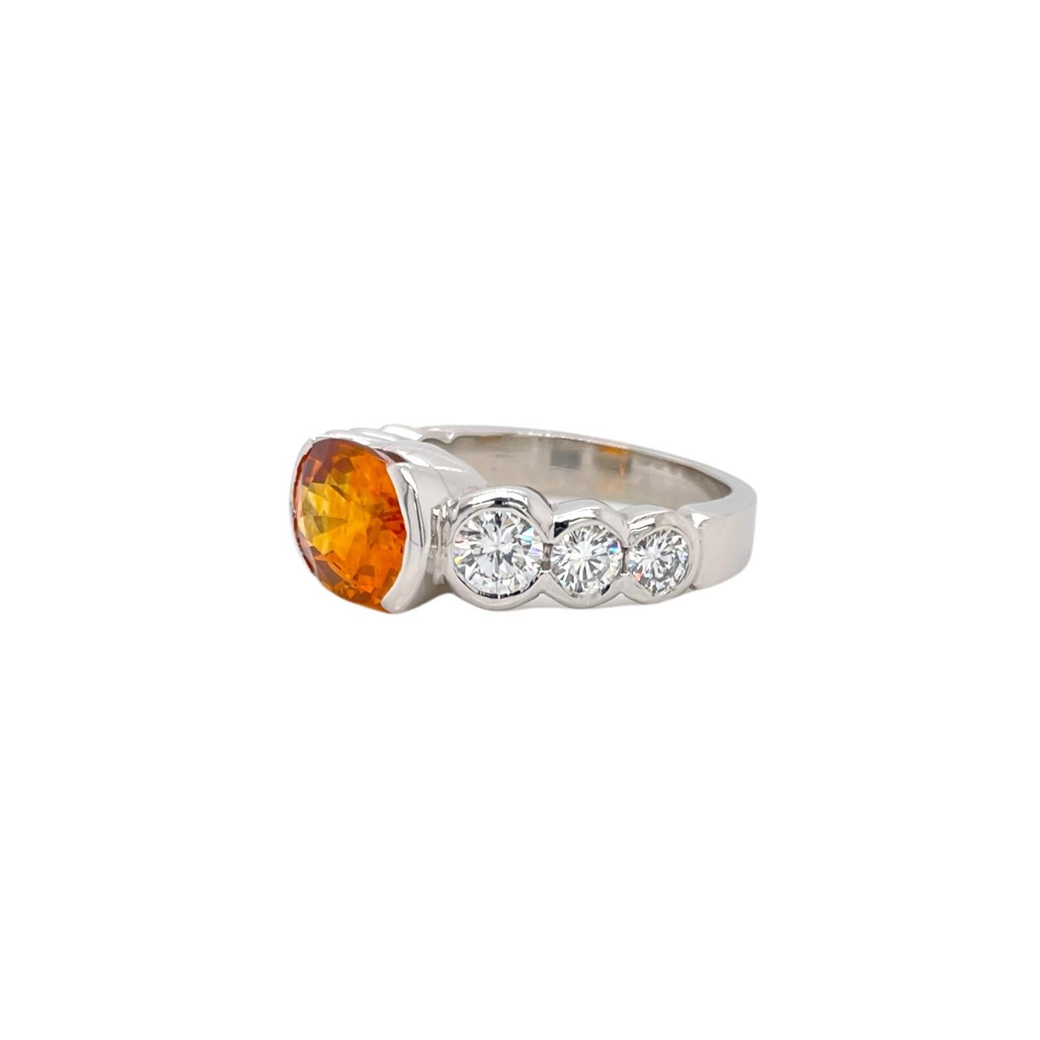Timeless orange sapphire and diamond ring in 18k white gold. Ring contains 1 center 9x7mm oval orange sapphire set in a half bezel weighing 3.12ct and 6 graduating round brilliant diamonds set in a full bezel weighing 0.91tcw. Diamonds are G in