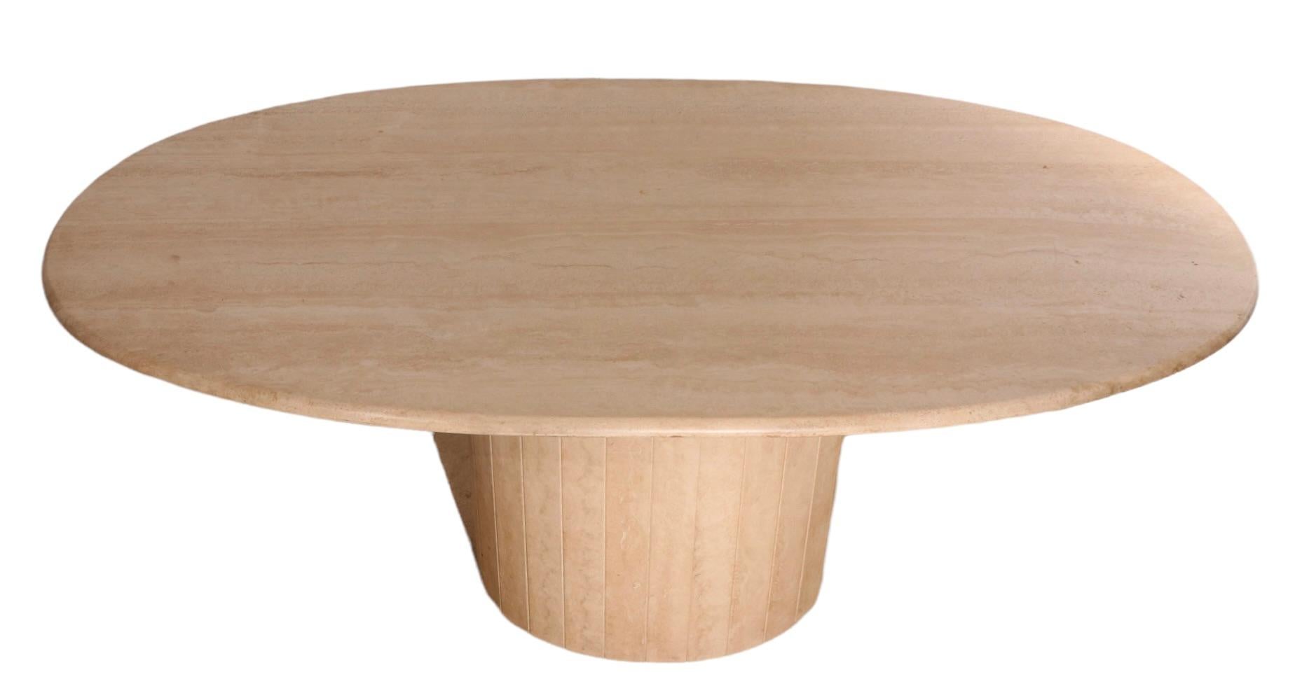 Super chic oval travertine marble dining table on segmented oval base. The table features a thick ( 1 in. ) top of solid marble, which has a rounded polished edge. The top rests on it’s original oval base ( 22.5 H x 25 W x 17.5 D in. )  which is