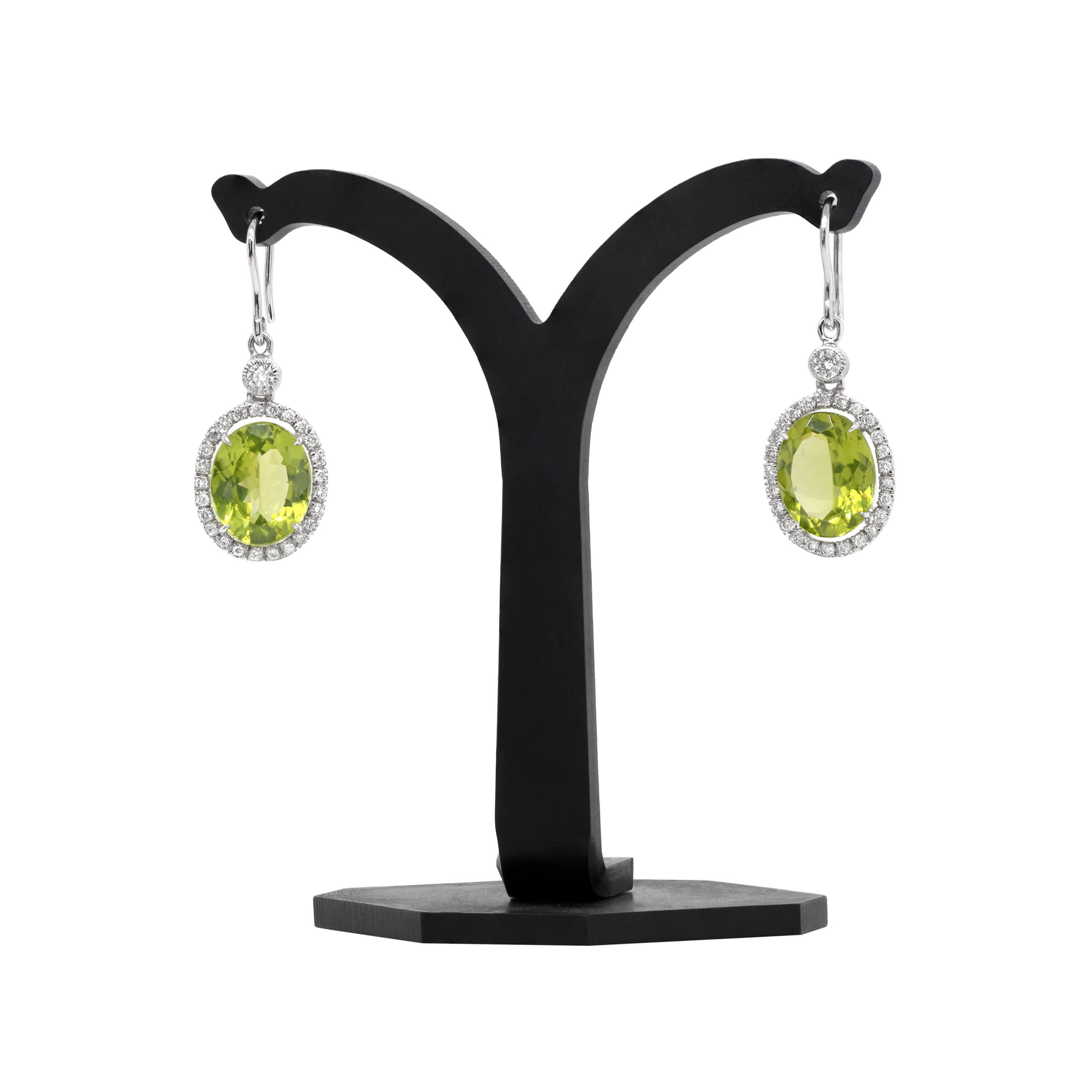 These incredible drop earrings feature an oval peridot gemstone weighing a combined 11.49 carats mounted in a four claw, open back setting. The vibrant stones are each beautifully surrounded by 25 claw set round brilliant cut diamonds. The oval