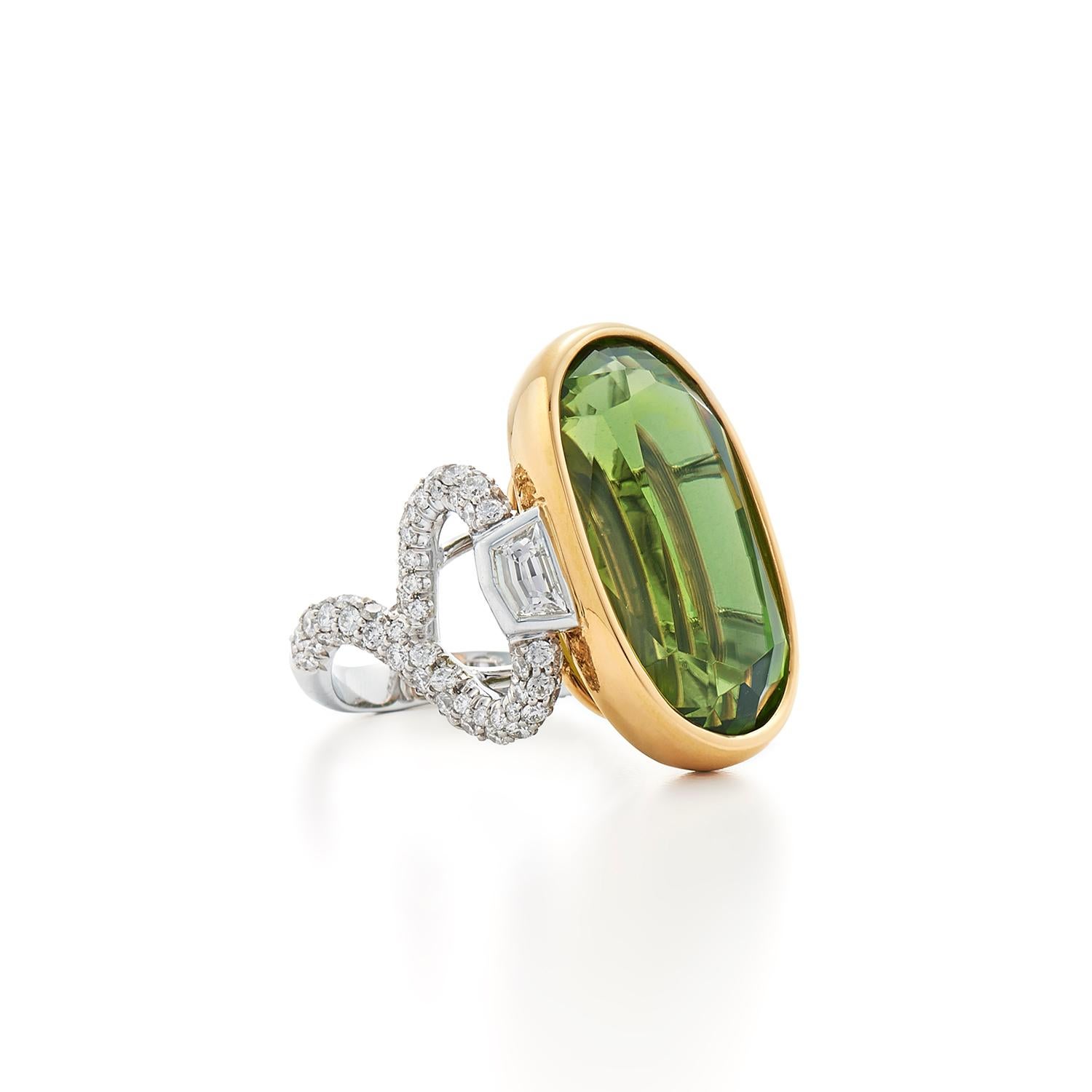 A fine oval peridot weighing 31.14 carats is set in a bezel of 18 karat yellow gold flanked with a pair of shield shape diamonds totaling approximately 0.67 carat atop a curving shank set with round diamonds totaling approximately 1.91 carats