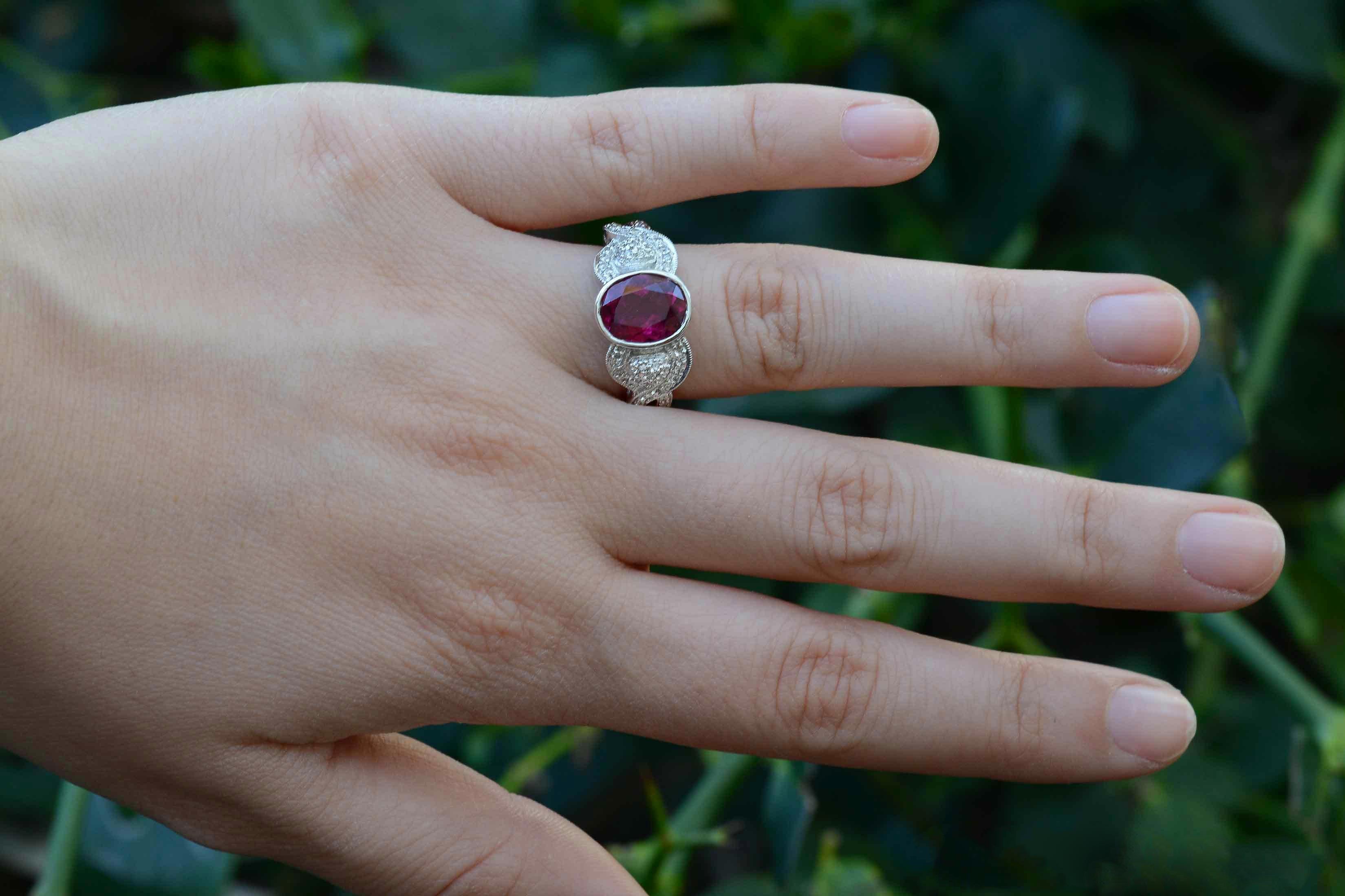 A most intriguing and vibrant, vintage pink tourmaline engagement ring set within a bezel is accompanied by a symphony of glimmering white diamonds in the crossover band. Lovingly crafted of 18K white gold, you'll love the way it sits low on your