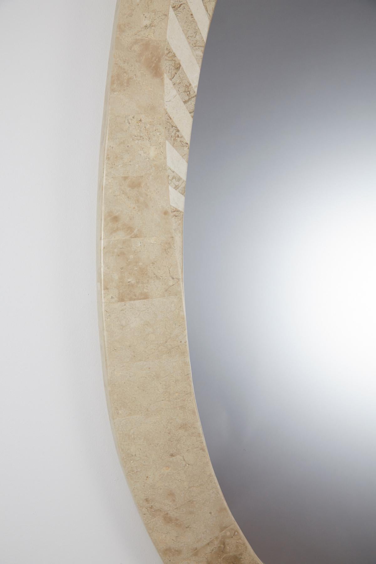 Oval-shaped mirror with frame completely covered in inlaid light beige fossil stone, with a broken pediment style connection between either side of the mirror. Each side is half- covered in stripes of white stone. Backed with painted wood. 

Pair