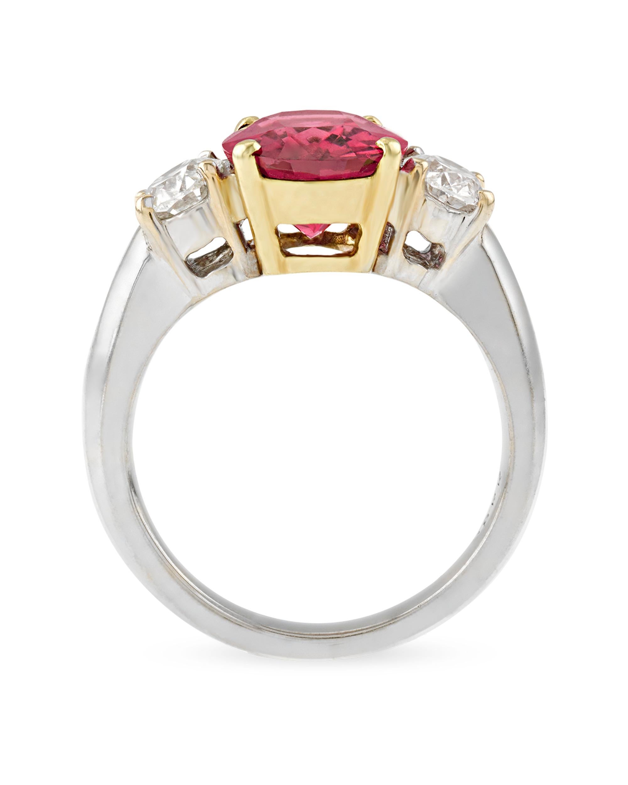 A sparkling red spinel captivates the eye in this ring. Exhibiting a stunning crimson color, this 3.76-carat jewel is set in 18K gold between two white diamonds totaling 1.04 carats. Though often mistaken for rubies or sapphires, spinels have