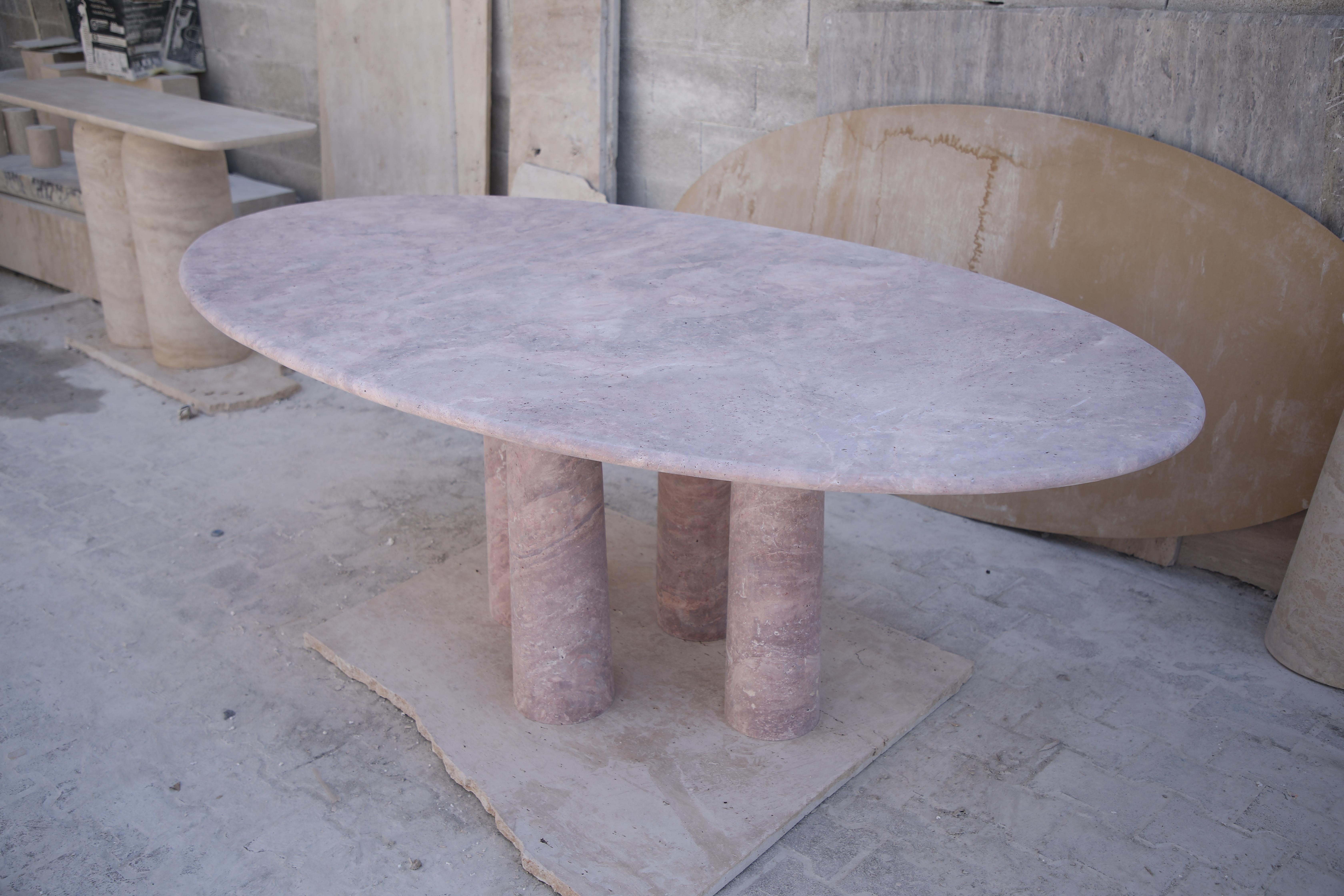 Cette table minimaliste est fabriquée à partir d'un seul matériau, un travertin rouge de haute qualité. Le plateau à bord incurvé repose élégamment sur quatre colonnes cylindriques légèrement effilées, ce qui confère à cette table un aspect