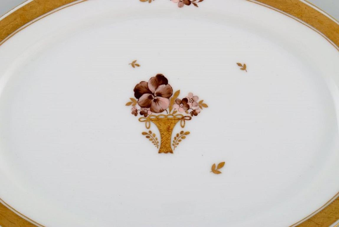 Ovale Royal Copenhagen Goldkorb Servierplatte aus Porzellan mit Blumen und Golddekor. 
Modellnummer 595/9008. Anfang des 20. Jahrhunderts.
Maße: 28.5 x 20 cm.
In ausgezeichnetem Zustand.
Gestempelt.
1. Fabrikqualität.