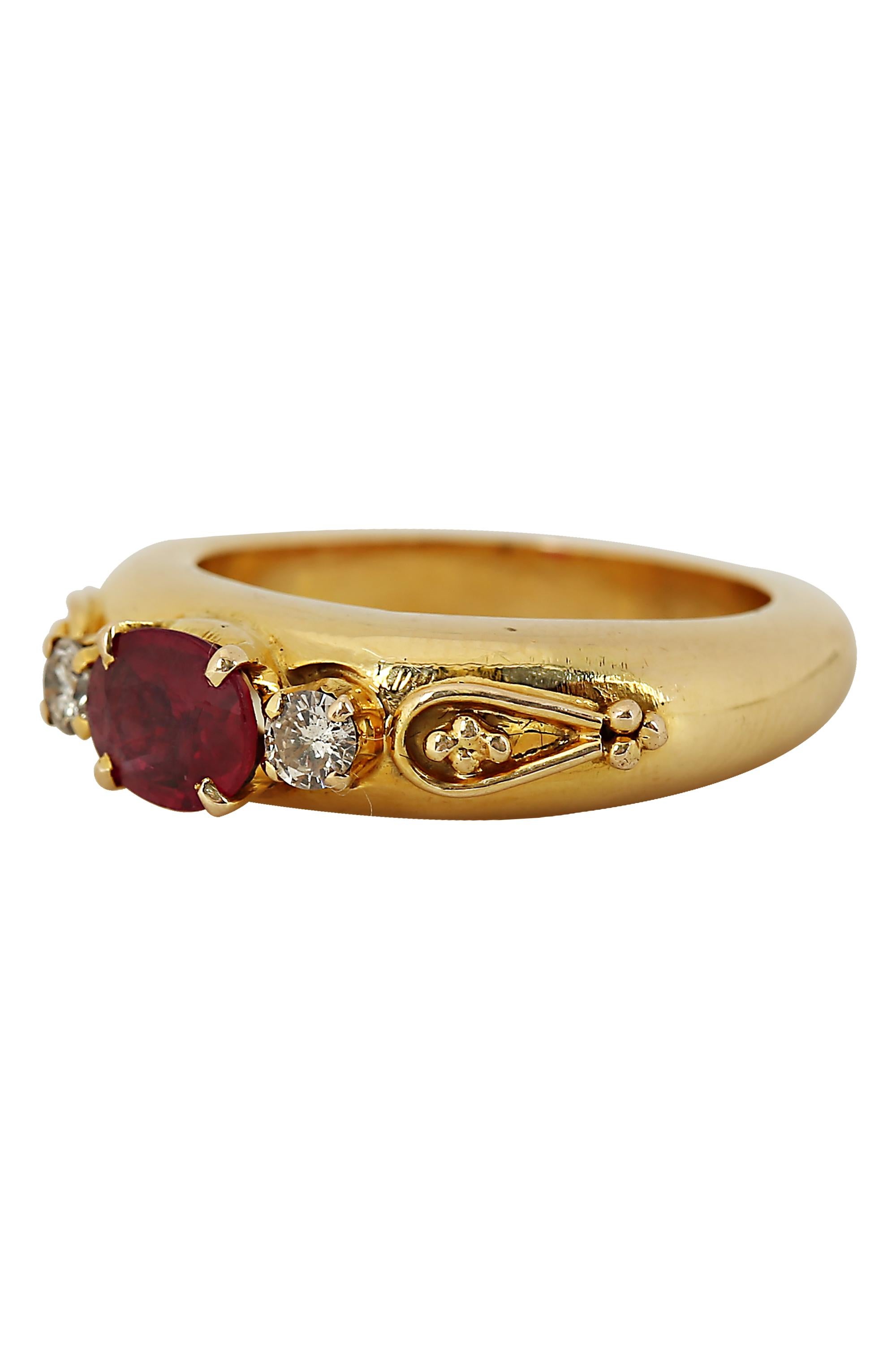 A bold ruby and diamond ring featuring a rich red oval ruby of approximately .65 carats illuminated by two round brilliant diamonds in a modern 18 karat yellow gold tubular setting highlighted by beadwork designs at the shoulders. Diamond weight is