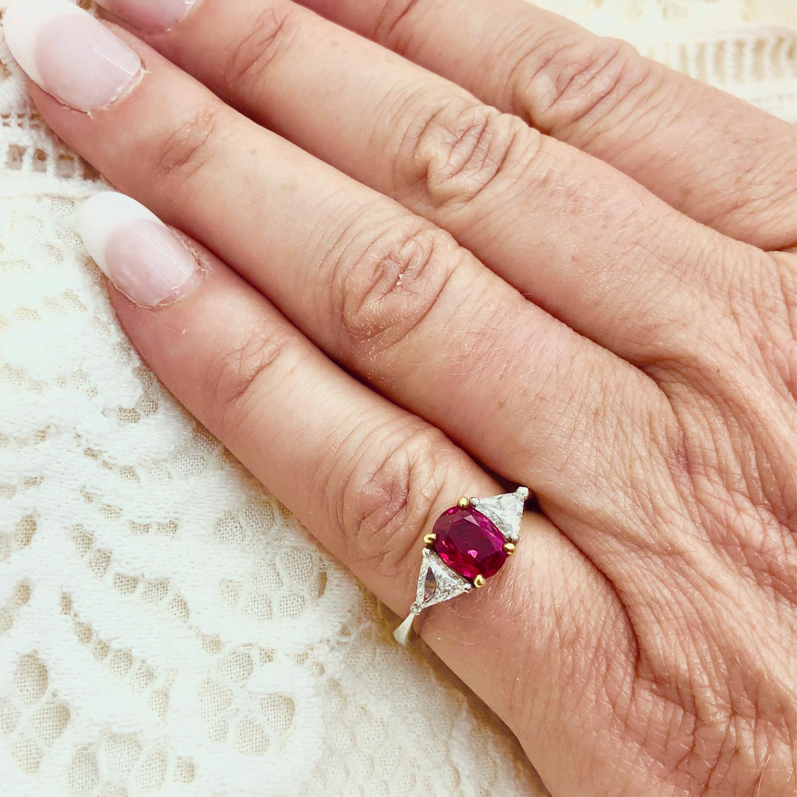 The ring features one 1.55 carat oval-shaped ruby flanked by 2 trilliant-cut diamonds, with a total approximate weight of 0.52 carats, in a platinum & 18k yellow gold setting. The weight of the ring is 5.9 grams and is a currently a size 6 1/2.