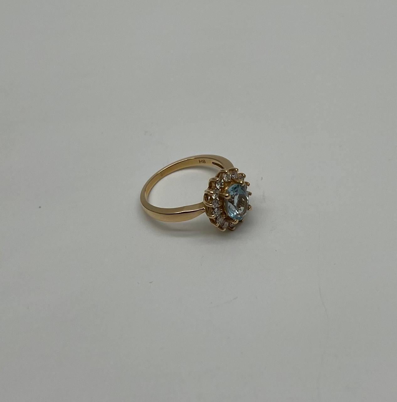 A refined and elegant ring featuring a central oval-shaped aquamarine gemstone, exuding a cool and serene blue hue. The aquamarine is encircled by a halo of round brilliant-cut diamonds, enhancing its brilliance and adding a touch of sparkle.