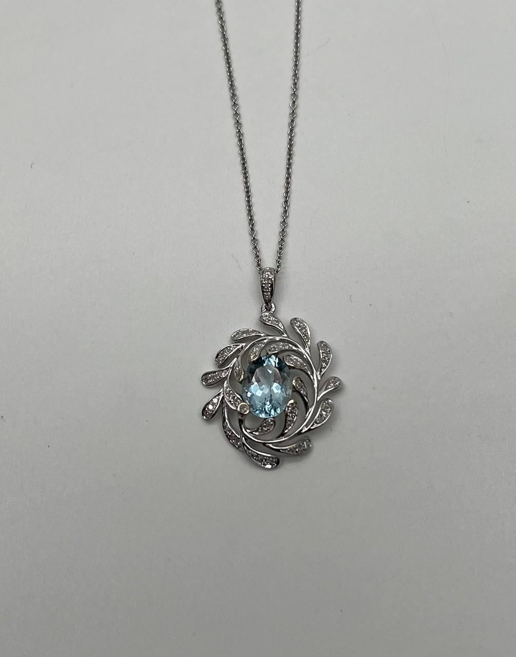 This elegant pendant necklace, features a captivating swirling open design. At its heart, a shimmering light blue aquamarines encircled by delicate, leaf-like accents adorned with sparkling diamonds. The intricate detailing adds a touch of