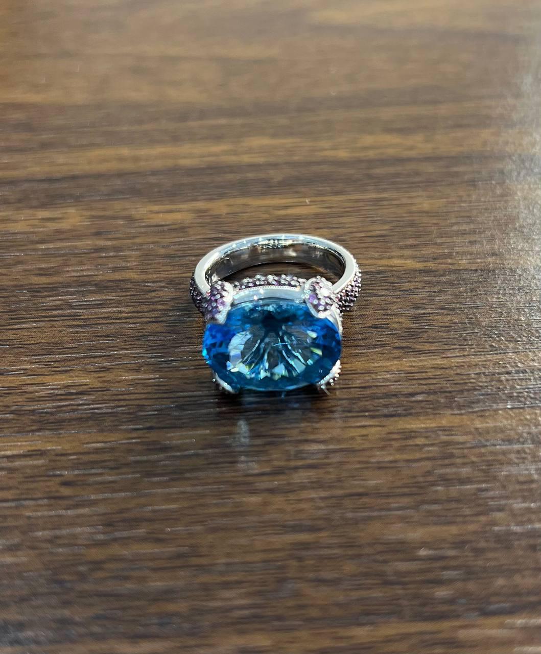 Experience the refined allure of this exquisite ring, a testament to modern craftsmanship.

The ring showcases a striking blue topaz, elegantly set in a polished 14K White Gold band. Flanking the central stone are pavé-set pink sapphires, adding a