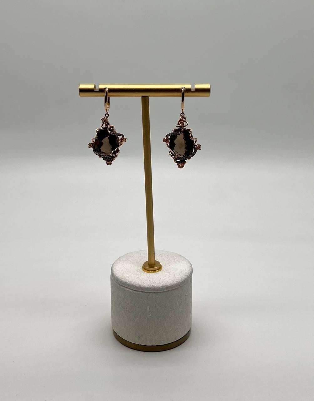 These distinctive earring features a dark, faceted brown smoky quartz set in a rose gold-toned frame. The frame is adorned with delicate, intricate detailing that enhances the gemstone's allure. The earrings are designed to dangle gracefully, adding