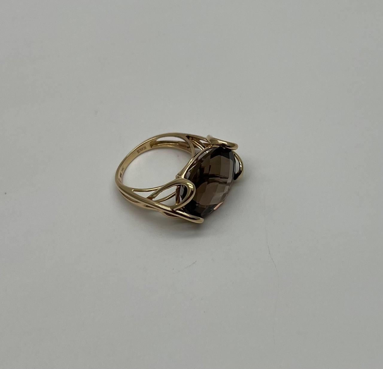 A study in elegance and form.
This striking ring features a captivating, faceted smoky quartz centerpiece. The oval stone is securely embraced by a delicate, openwork gold setting, enhancing its natural allure. The band, crafted with smooth curves,
