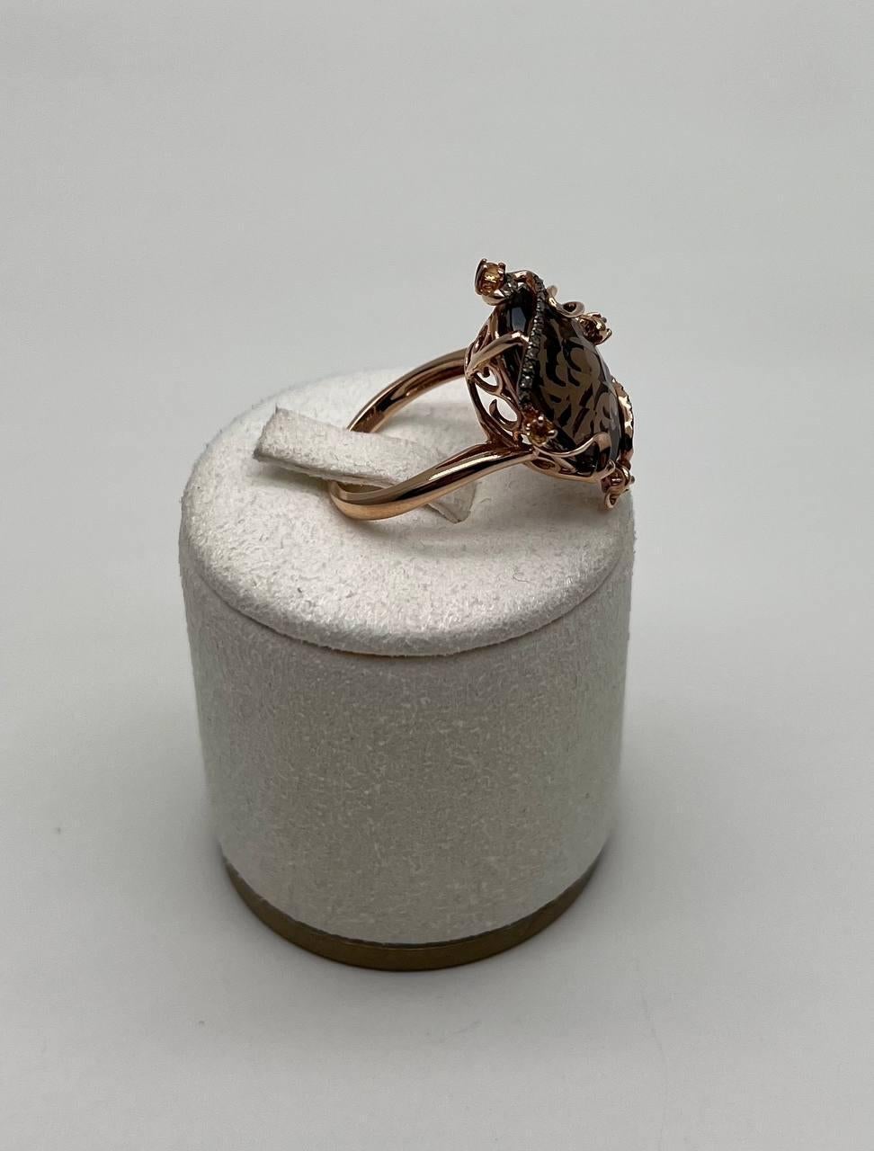 Cette bague exquise présente un grand quartz fumé brun foncé facetté, serti dans une monture complexe en or rose. Le design comprend des tourbillons et des accents délicats qui s'enroulent autour de la pierre, ajoutant une touche de sophistication.