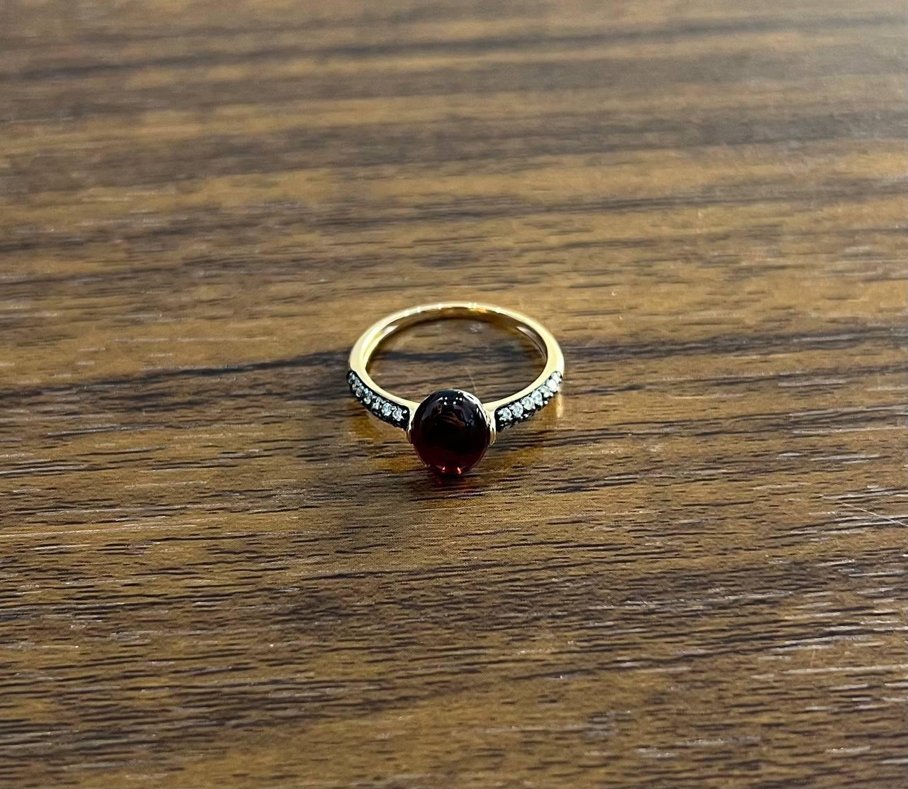 A striking ring featuring a red cabochon ruby set in a band adorned with small diamonds. Mounted in a sleek 14k Yellow gold setting.