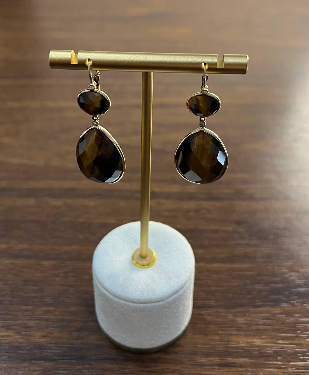 These elegant earrings feature faceted dark brown sapphires set in a sleek 14k gold frame.
Each earring showcases a smaller round stone above a larger teardrop-shaped stone, both with a rich, deep hue.
The stones are expertly cut to enhance their
