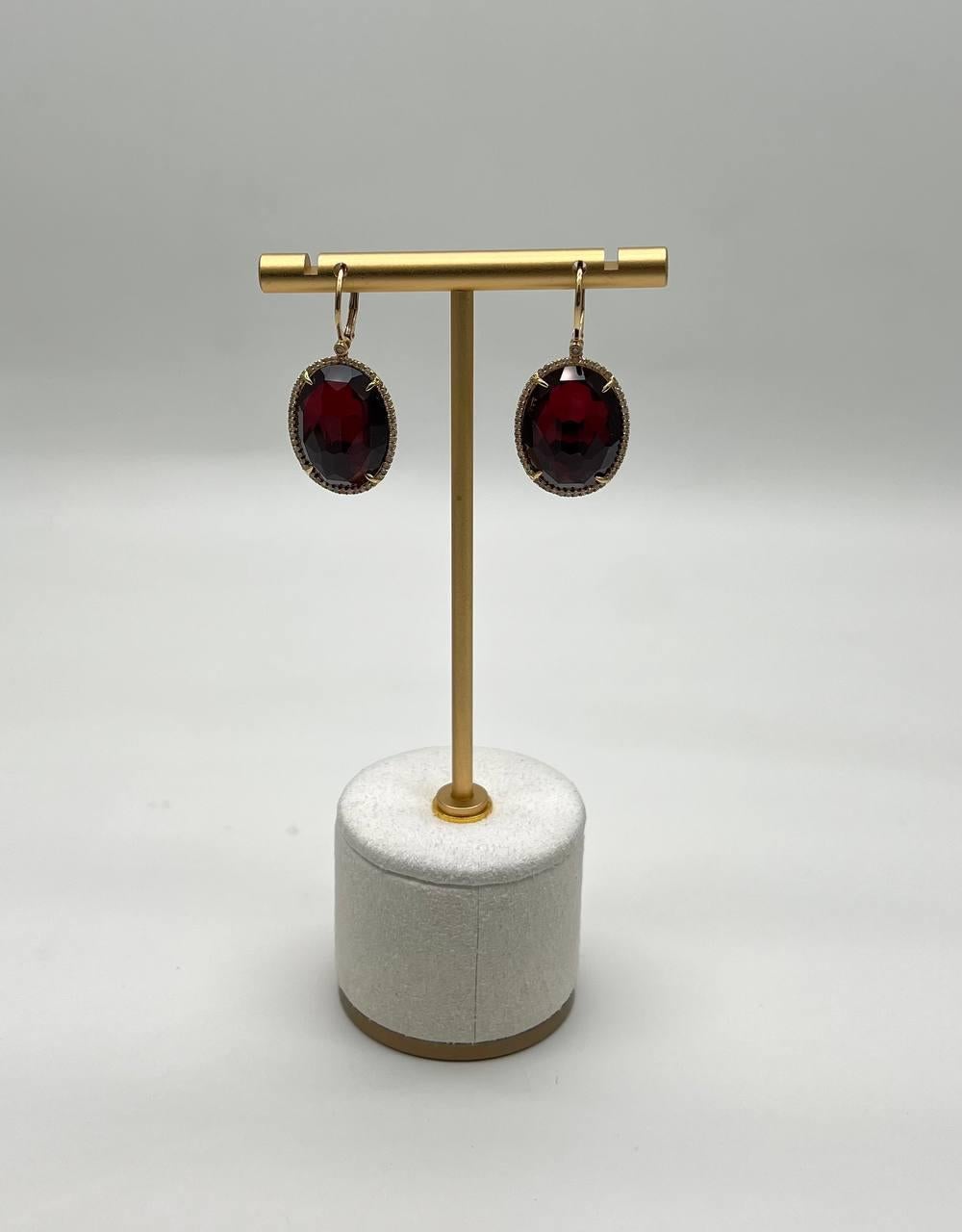 Elegantes Pendientes de Oro de 14K con Zafiro Rojo Oscuro de 20 X 15MM y Diamantes. Estos impresionantes pendientes llevan piedras de zafiro rojo intenso, bellamente facetadas y engastadas en oro de 14k. Cada piedra está rodeada por un delicado halo