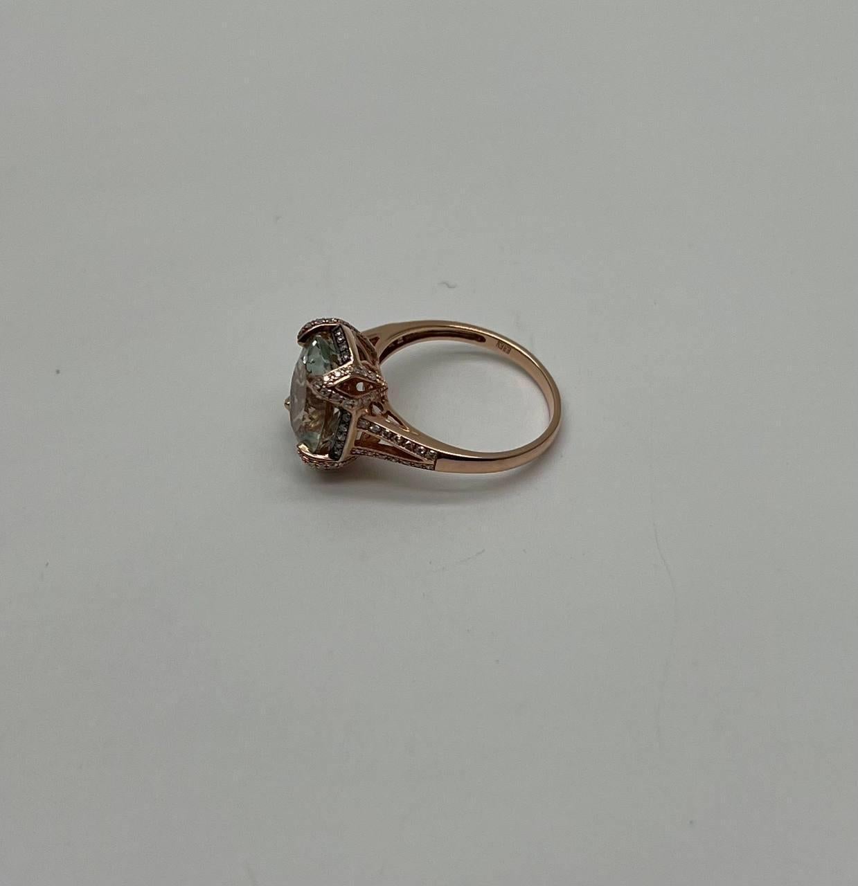Un anello sofisticato con una grande ametista verde (Prasiolite) dal taglio a cuscino e un'aureola di diamanti chiari e scintillanti.
L'anello è impreziosito da piccoli diamanti rotondi incastonati lungo la fascia, che esaltano la brillantezza della