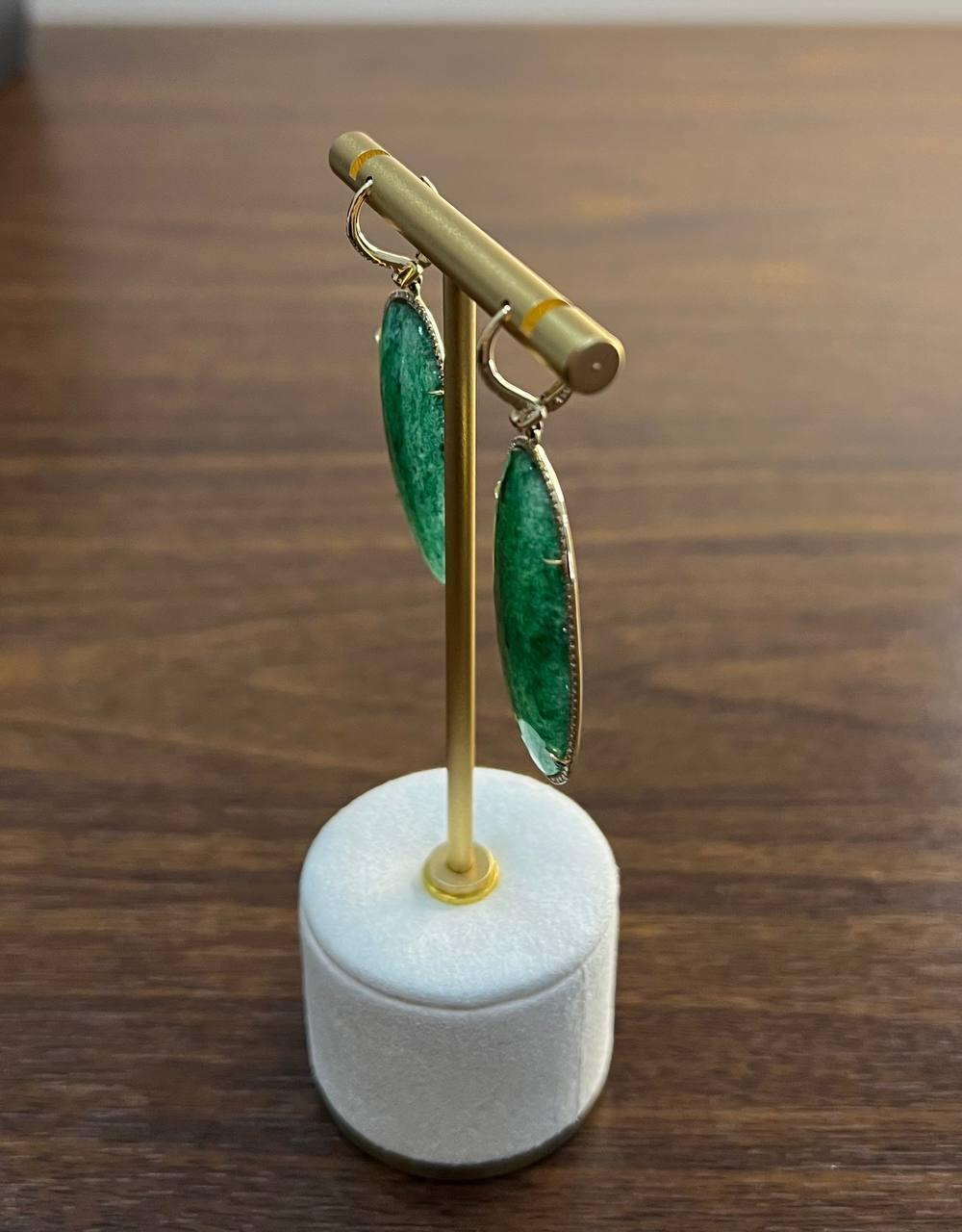 Estos llamativos pendientes presentan una gran Aventurina verde de forma ovalada, elegantemente enmarcada y suspendida de delicados ganchos. Las piedras presentan un tono verde intenso con variaciones naturales, lo que añade profundidad y carácter