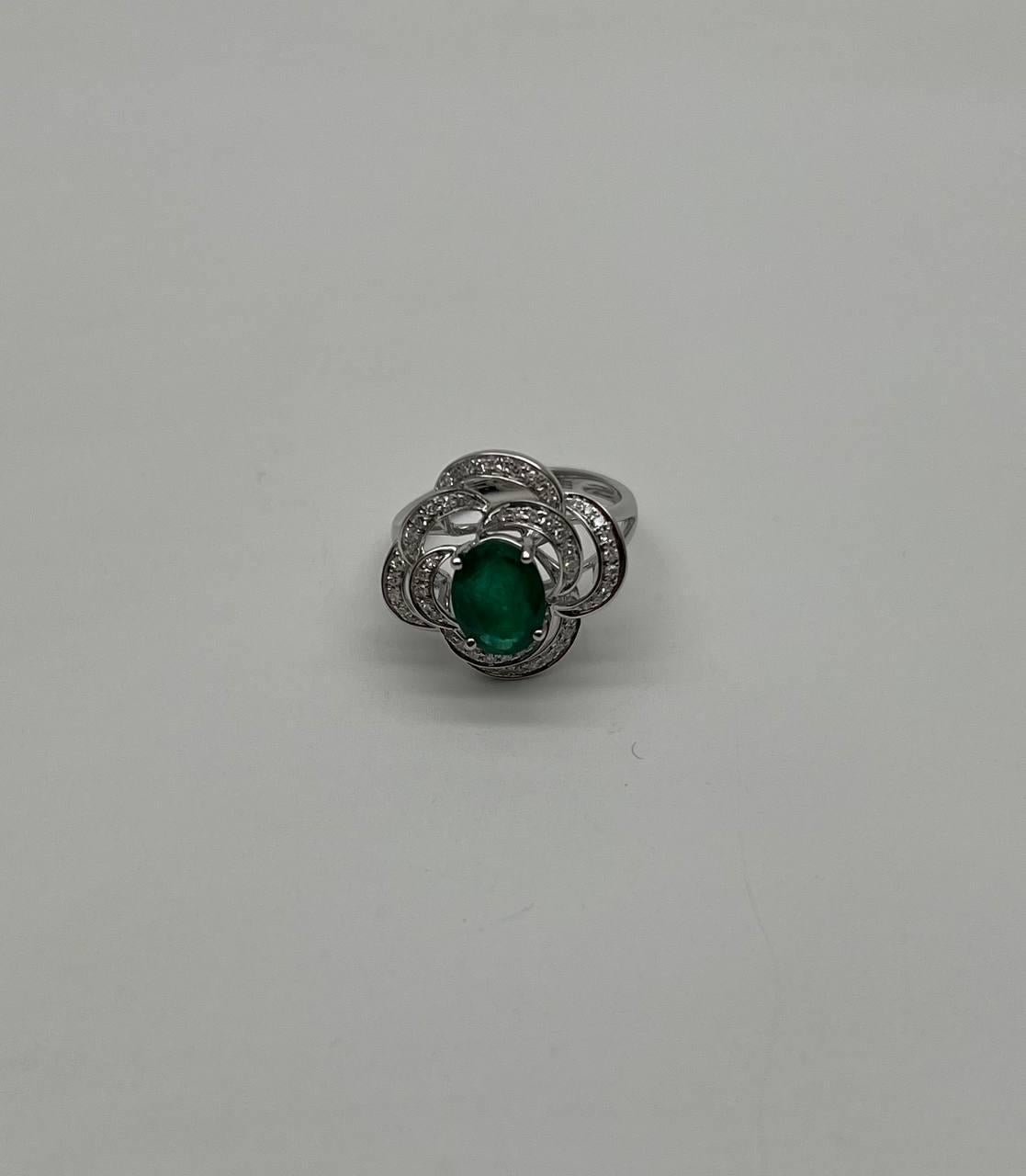 This exquisite ring features a vibrant green emerald at its center, elegantly encircled by intricate loops of sparkling diamonds. The diamonds are meticulously set in a swirling pattern, enhancing the ring's captivating design. The emerald is