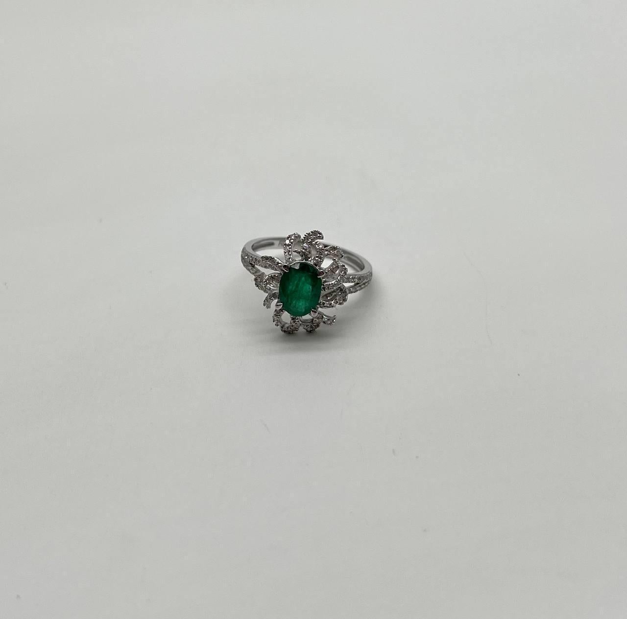 A stunning emerald ring. This exquisite piece  features a captivating design. The ring showcases a central oval emerald, surrounded by an intricate arrangement of sparkling diamonds. The setting is crafted in a way that enhances the brilliance of