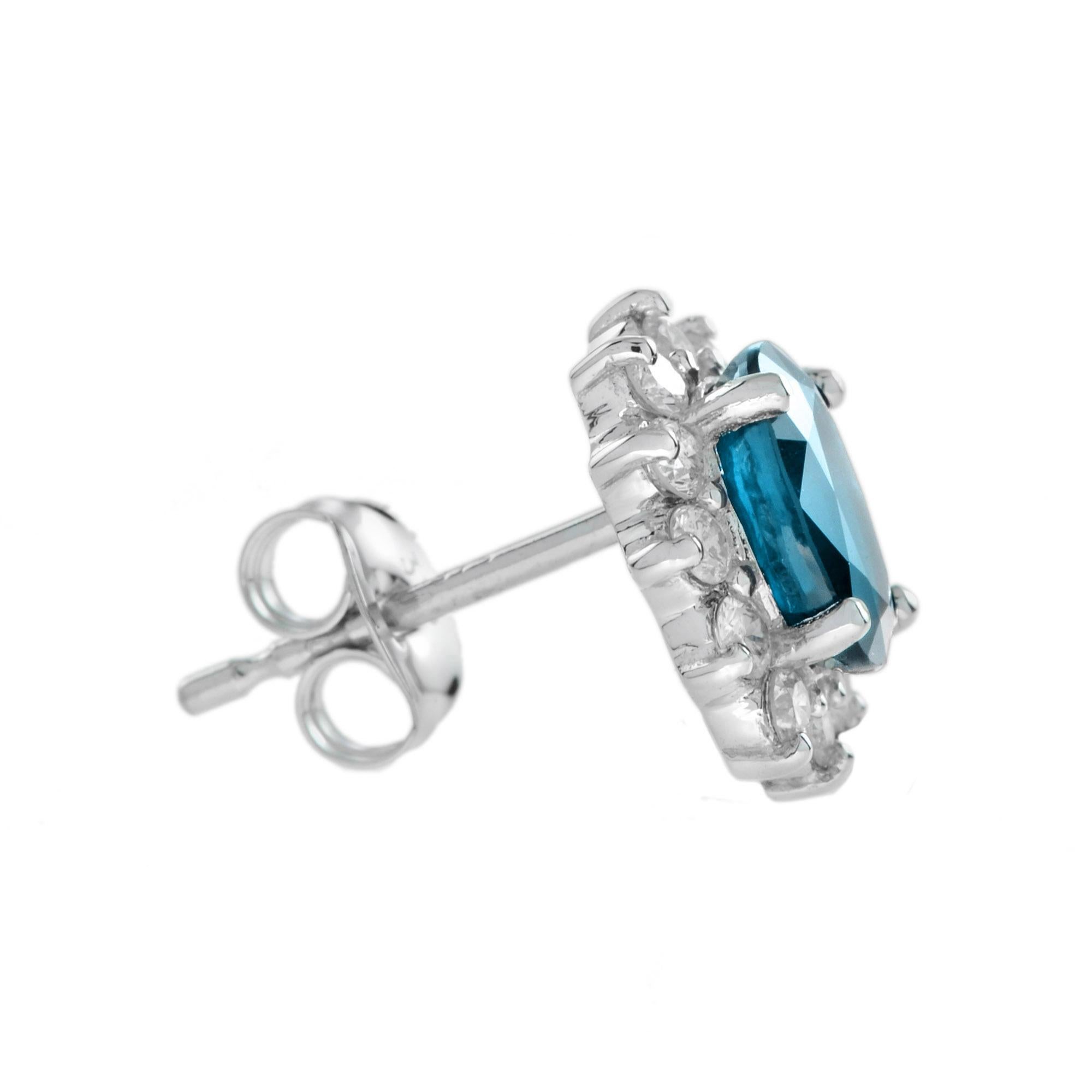 Ein Paar ovale Londoner Blautopas- und Diamantcluster-Ohrringe. Jeder Ohrring besteht aus einem ovalen Blautopas, der von zwölf runden Diamanten im Brillantschliff umgeben ist. 14K Weißgold. 
Ohrringe Informationen
Breite: 9 mm.
Länge: 11