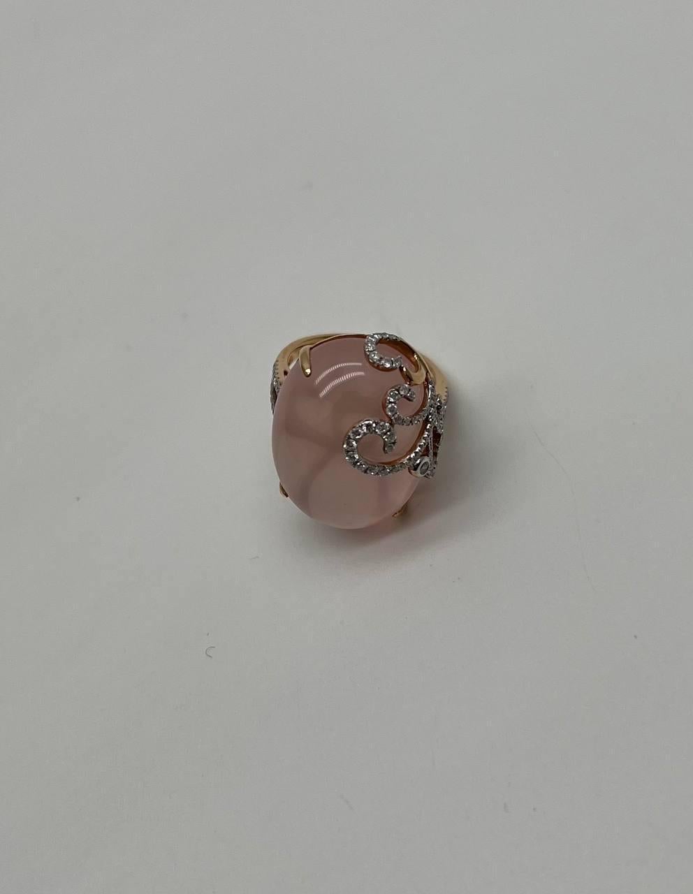 This exquisite ring features a polished pink rose quartz oval cabochon set in a delicate gold prong setting. The stone is adorned with an intricate swirl of sparkling accent diamonds, adding a touch of elegance. 18K White Rose Gold.  24.73 Cts Pink