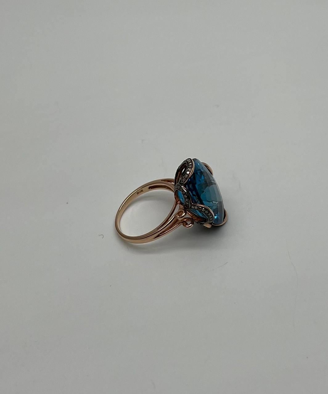 A striking ring featuring a large 19.2 carat oval-shaped blue topaz of a deep and captivating blue color. The ring is accented by 0.22 carats of champagne-colored diamonds, adding a subtle sparkle around the topaz. Crafted in 14k rose gold.