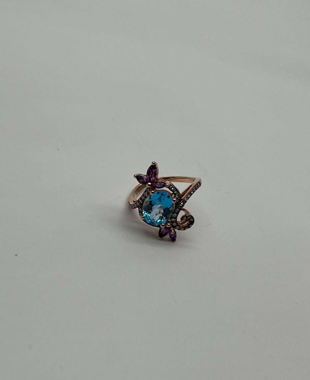 Elegant 14k Rose Gold Blue Topaz and Amethyst Ring. This exquisite ring is crafted in 14k rose gold. The center features a stunning oval-cut blue topaz, surrounded by intricate detailing. Accents of amethyst add a touch of vibrant color,