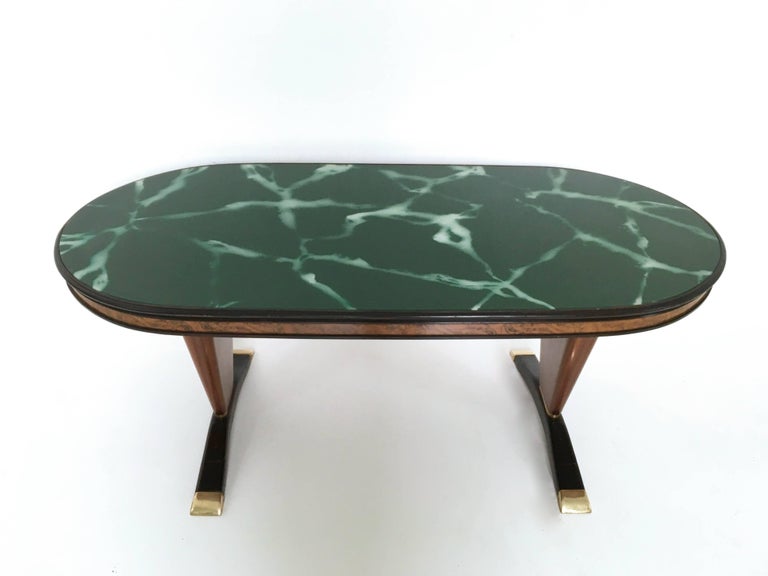 1950s.
This dining table is made in mahogany and ebonized wood and features brass details and a back-painted glass top with a marble effect. 
It is a vintage item, therefore it might show slight traces of use, but it can be considered as in very