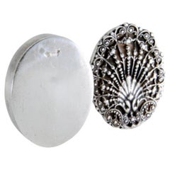 Oval-shaped silver pill box with raised plant motifs on the removable lid