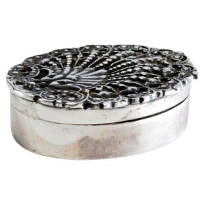 Oval-shaped silver pill box with raised plant motifs on the removable lid