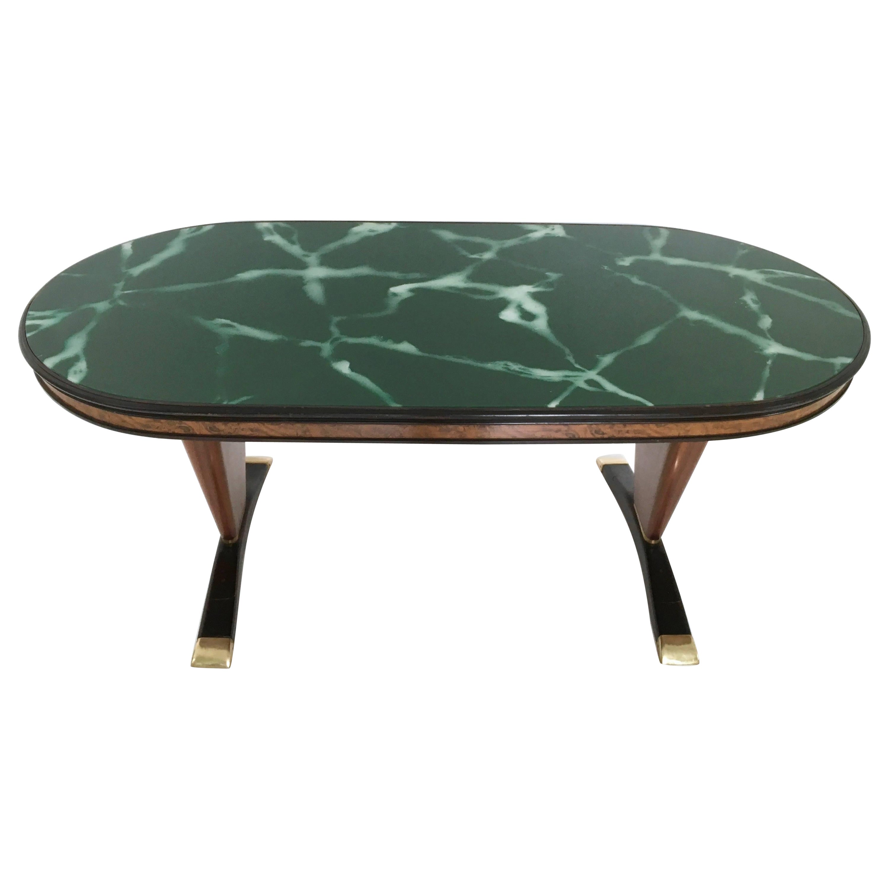 Made in Italy, 1950s.
This dining table is made in wood and ebonized wood and features brass details and a back-painted glass top with a marble effect. 
It is a vintage item, therefore it might show slight traces of use, but it can be considered as