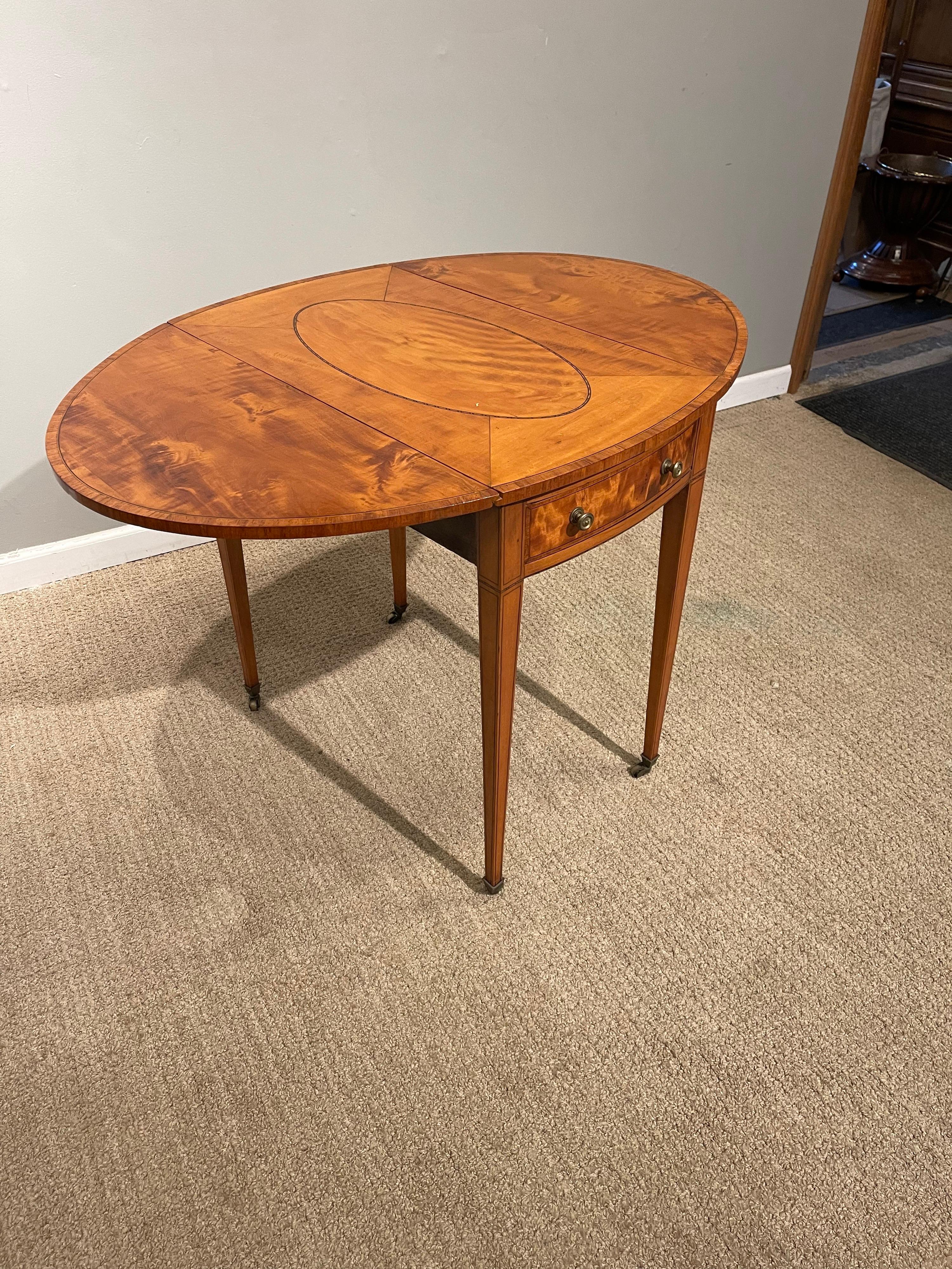 Stark gemaserter ovaler Pembroke-Tisch aus Sheraton-Satinholz
mit einem ovalen Medaillon im oberen Teil, das mit Satinholz umrandet ist &
mit Ebenholzbespannung. Erhoben auf quadratischen, sich verjüngenden Beinen
Messing-Rollen &