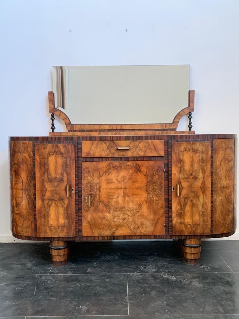 Splendid oval sideboard with mirror made of select walnut burl and framed in Macassar ebony with slight reliefs or protrusions on the body of the sideboard. The cabinet rests on two three-tier plinths finished in Macassar and briarwood complemented