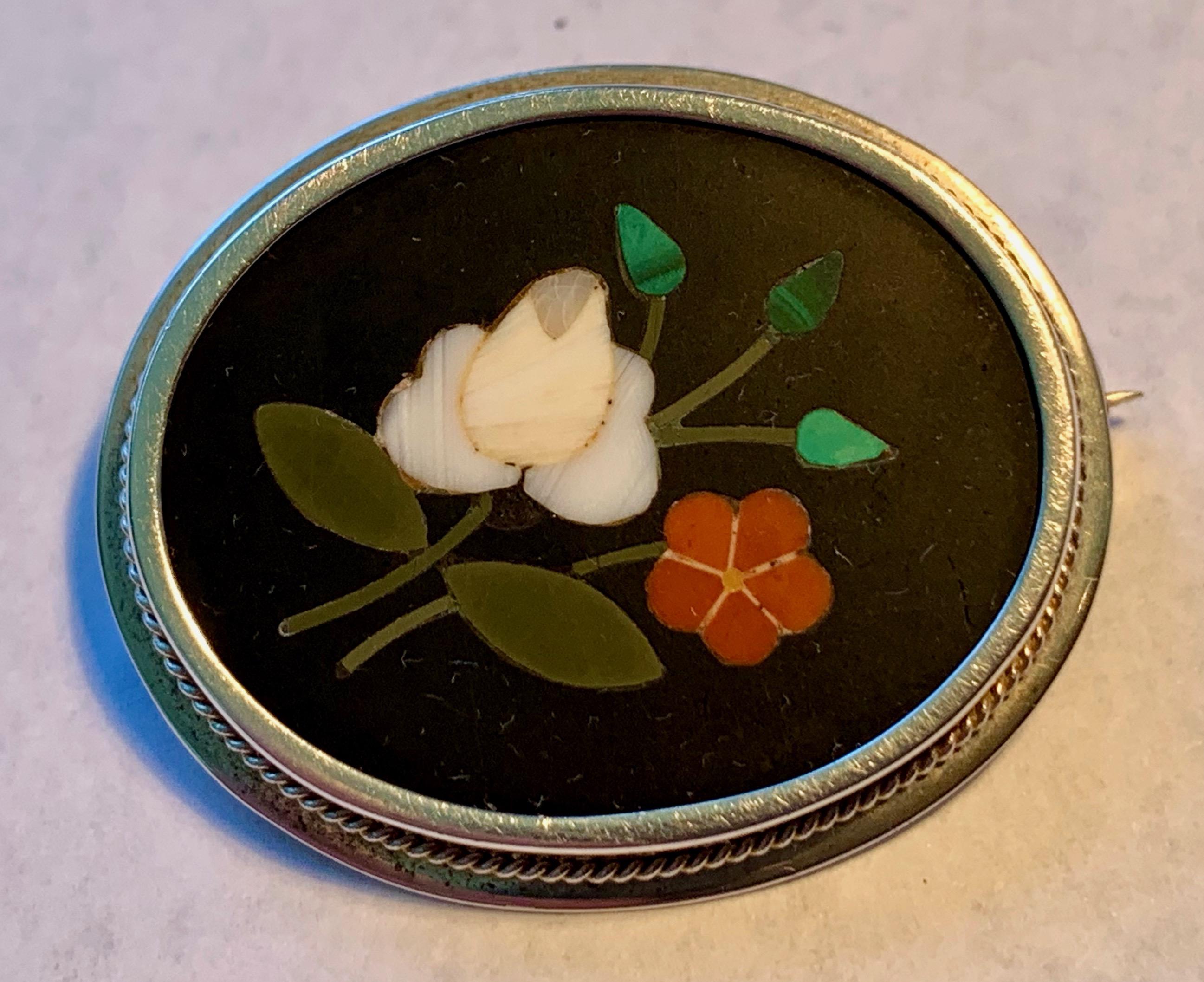 Victorian oval .800 silver pietra dura brooch with a pin stem locking back.  The black ground shows off a white rose with buds and another flower.   Simple and sweet.  The dark ground is black marble inlaid with hardstones and various semi-precious