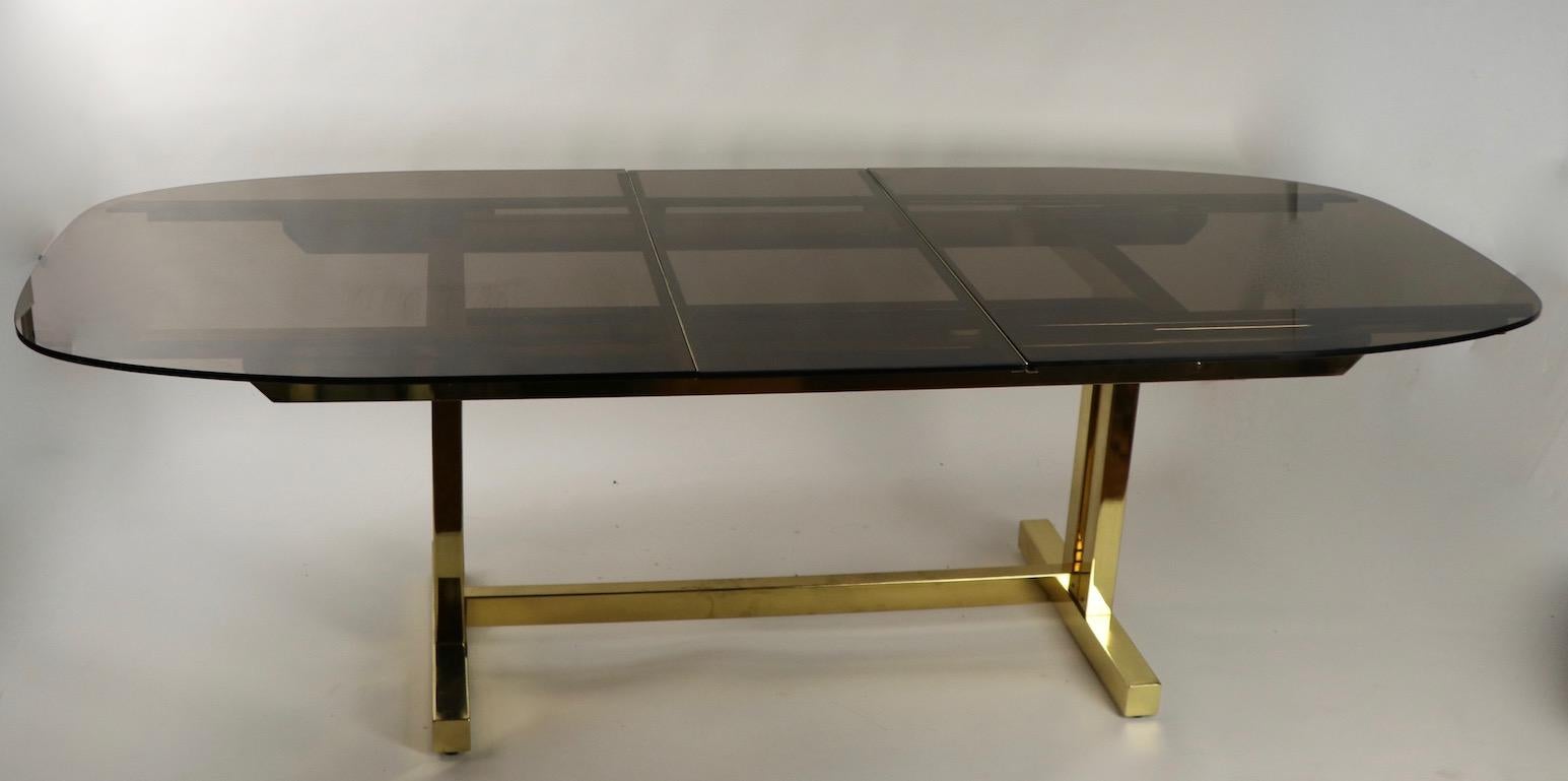 Impressive Postmodern, Art Deco Revival dining table of brass and smoked glass. This unusual table is extendable, having a 18 inch W leaf which stores under the glass surface when table is closed. Total W with leaf in place 95.25 x 77.5 W when